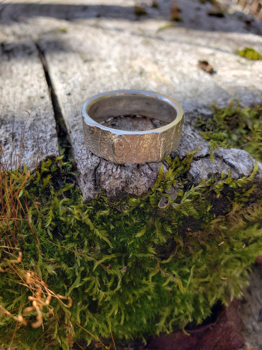 Silver ring with bark texture sitting on a mossy wooden board