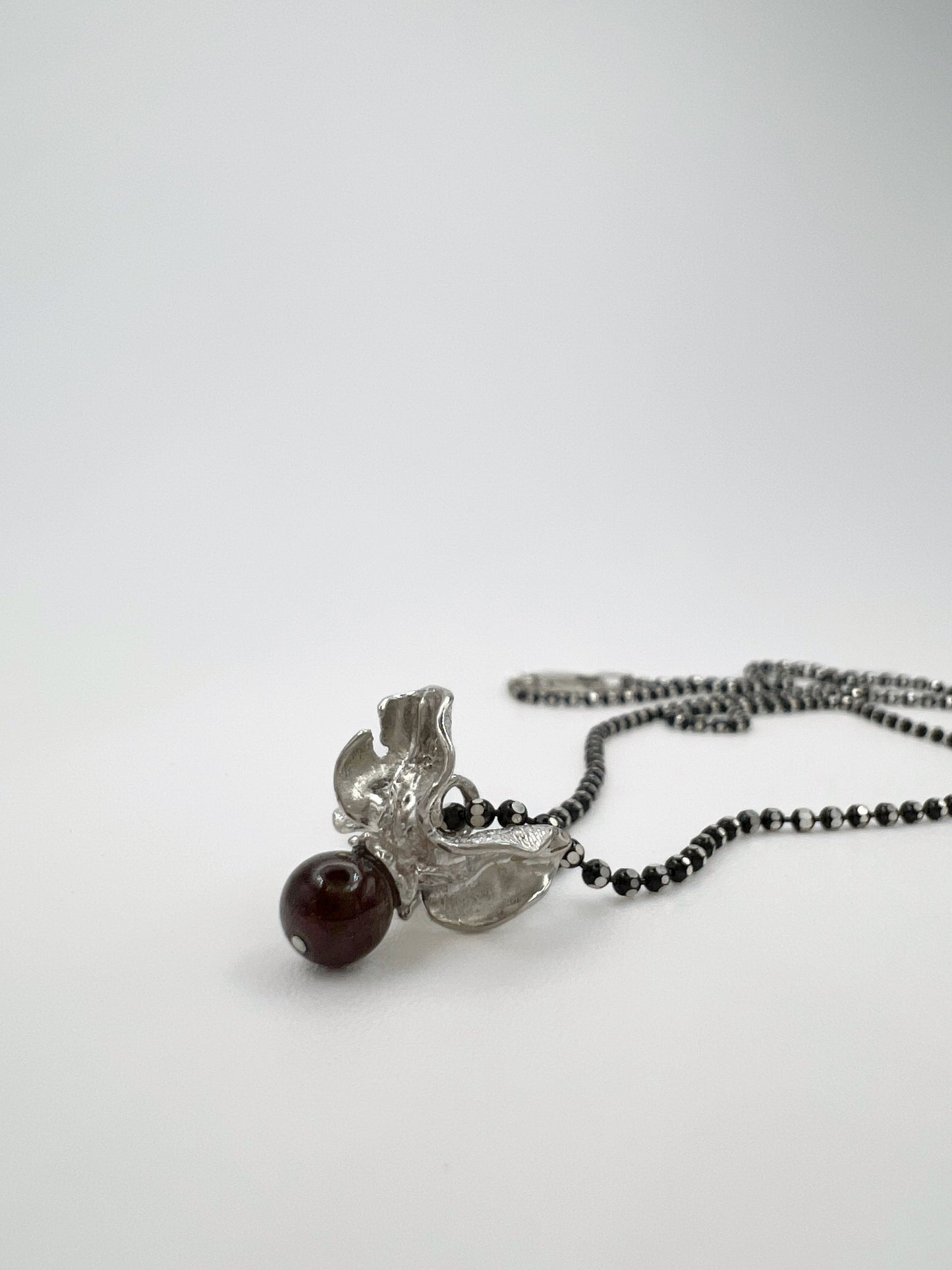 Silver pendant with a garnet bead on a fine cable chain. The garnet is such a deep red that it appears black. The pendant is shaped like the shell & berry from a bittersweet vine. Displayed against a white background.
