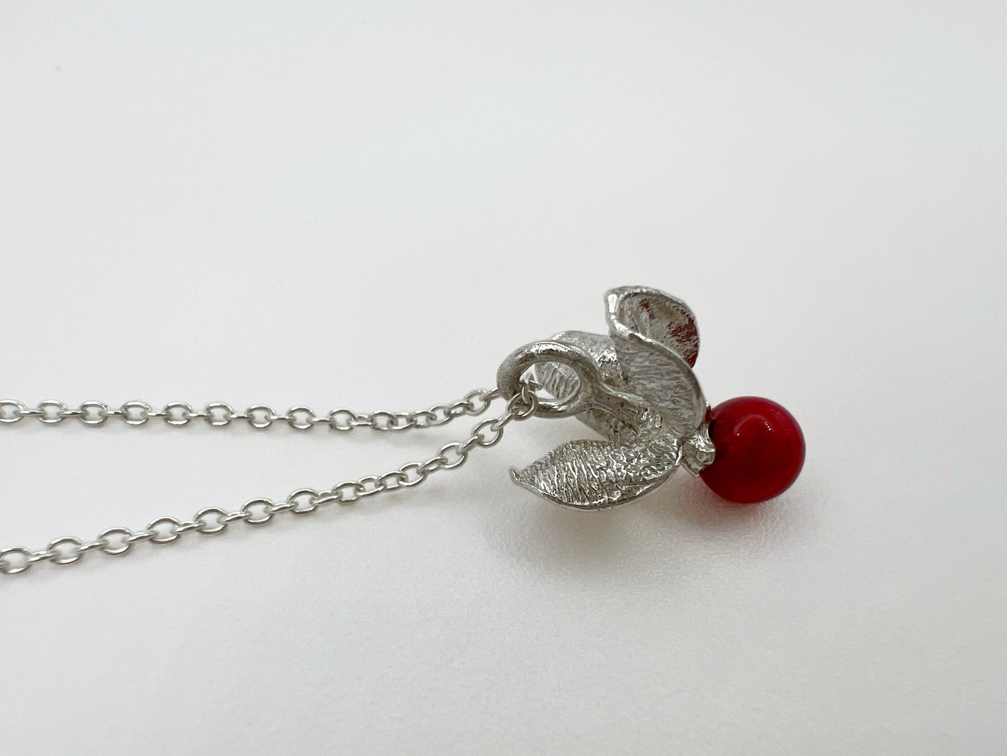 Silver pendant with a red sea bamboo bead on a fine cable chain. . The pendant is shaped like the shell & berry from a bittersweet vine. Displayed against a white background.