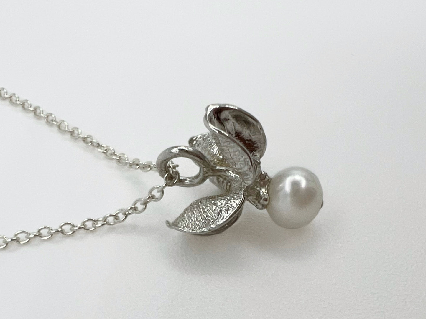 Silver pendant with a white pearl on a fine cable chain. . The pendant is shaped like the shell & berry from a bittersweet vine. Displayed against a white background.