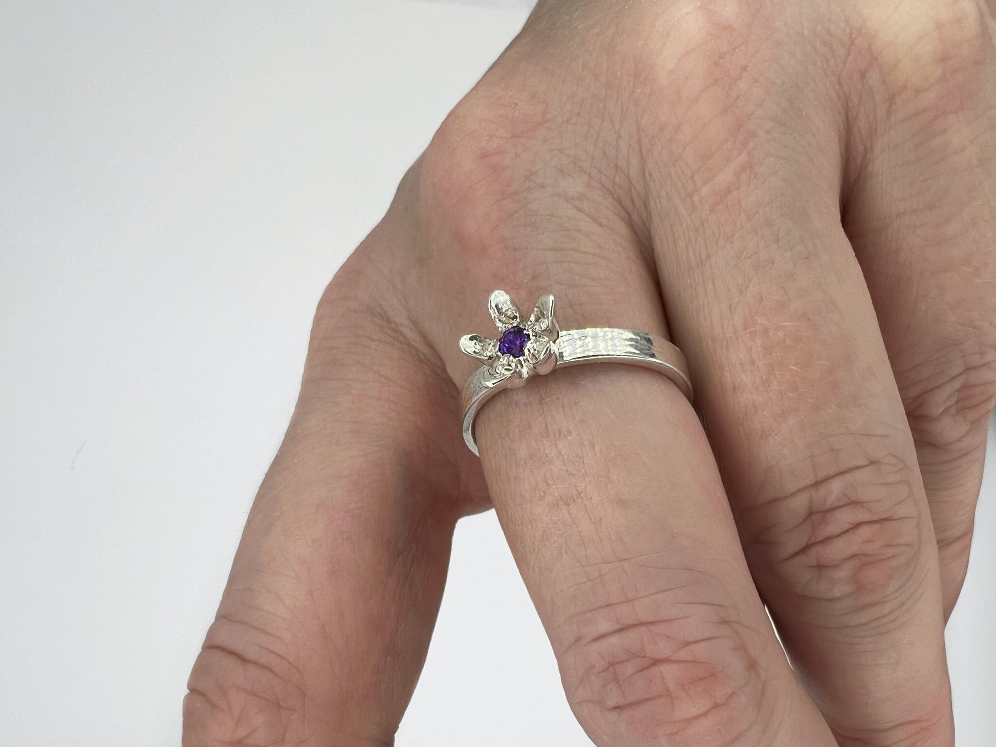 silver ring with milkweed flower and amethyst center, worn on a hand