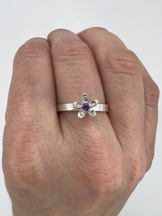 silver ring with milkweed flower and amethyst center, worn on a hand