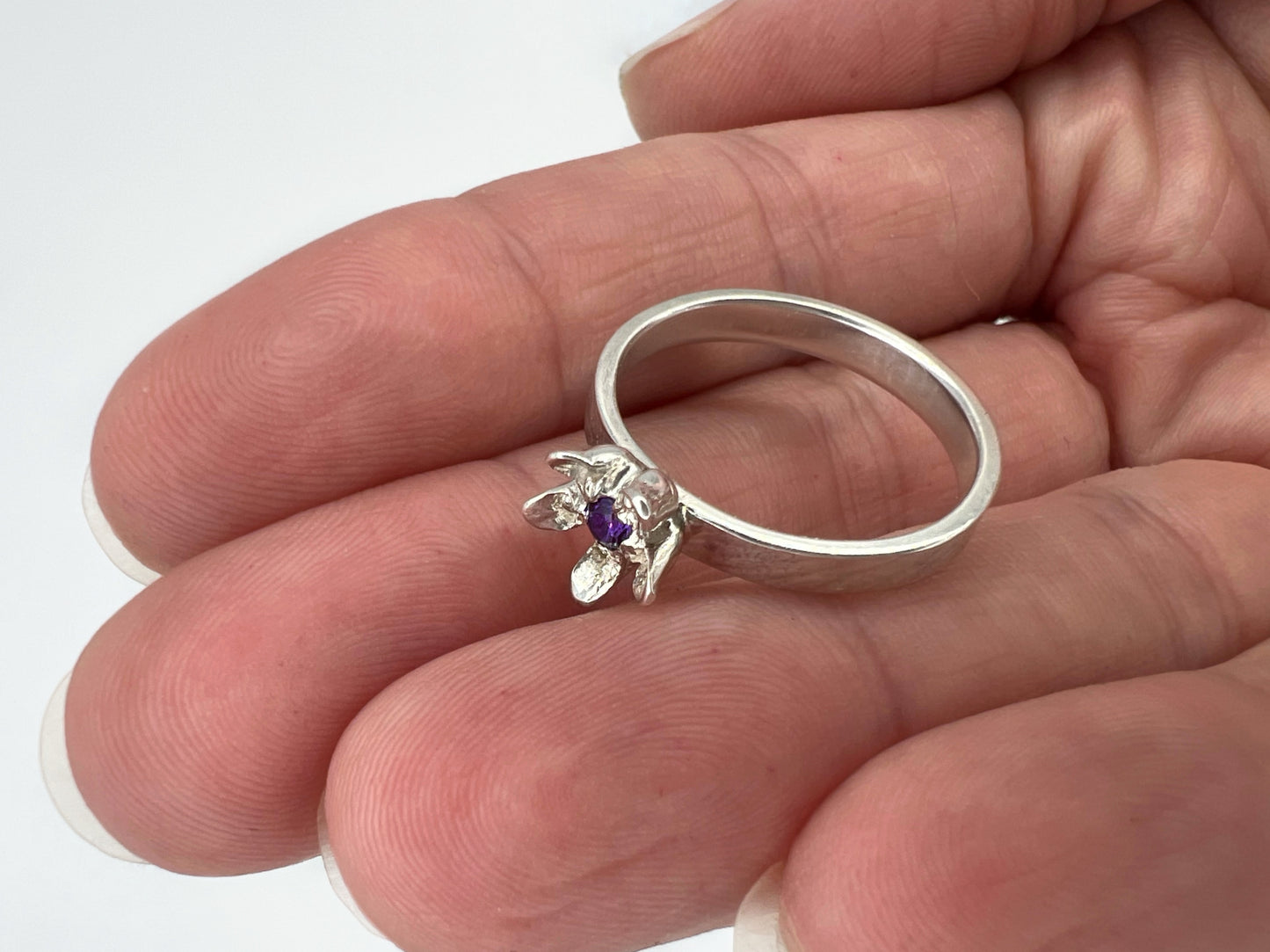 silver ring with milkweed flower and amethyst center, held in a hand