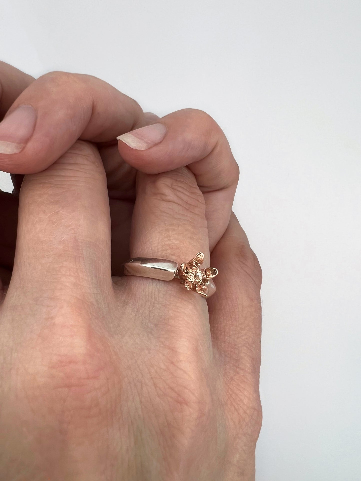 Clasped hands wearing a ring with sterling silver band shaped like a leaf with a pink gold milkweed flower rising from between the "leaves"