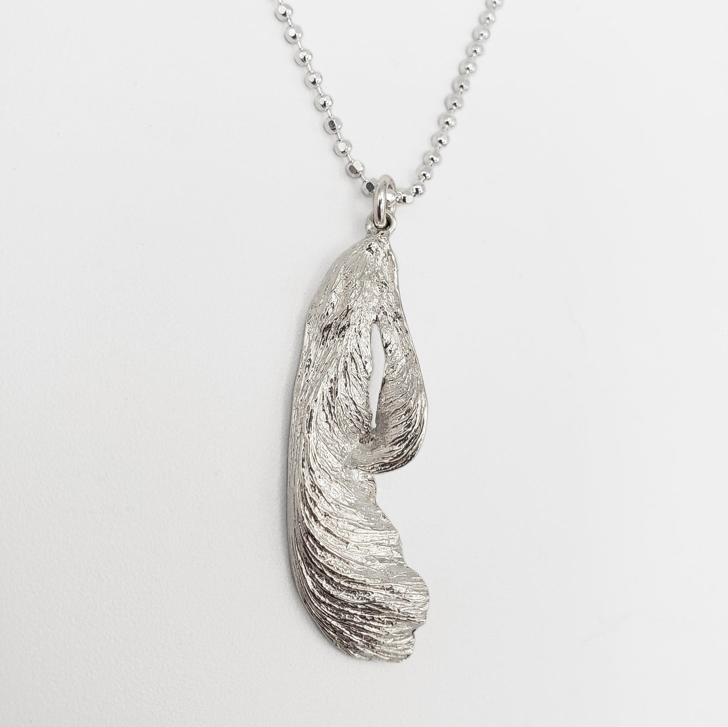 A silver maple key pendant on a white background.