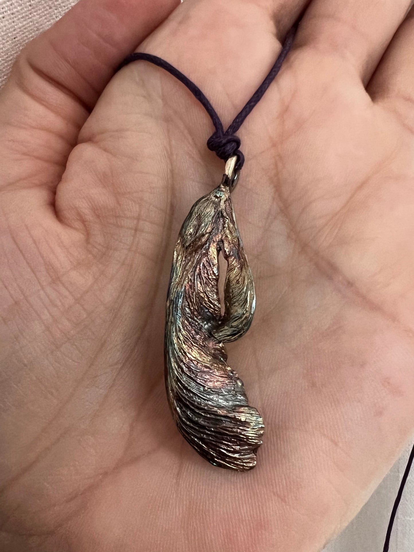 An oxidized silver maple key pendant on purple waxed cotton cord in the palm of a hand.