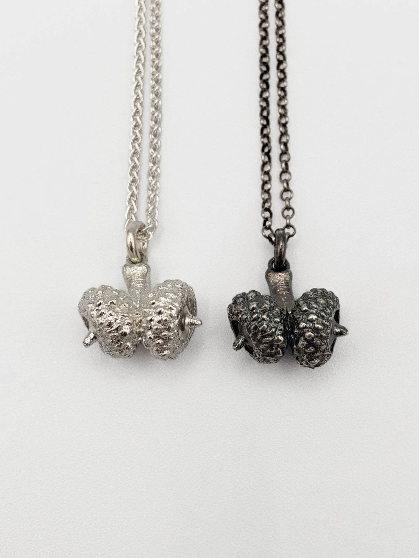 Two silver double acorn pendants. One silver colour, the other oxidized grey colour