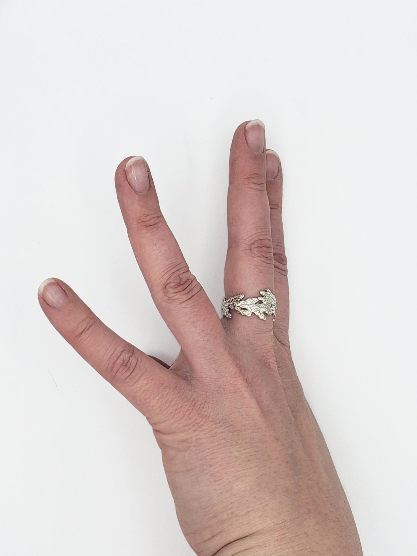 Hand wearing wide sterling silver cedar ring, shown from a sideways angle with fingers spread.