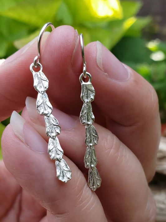Hand holding sterling silver cedar stick earrings.