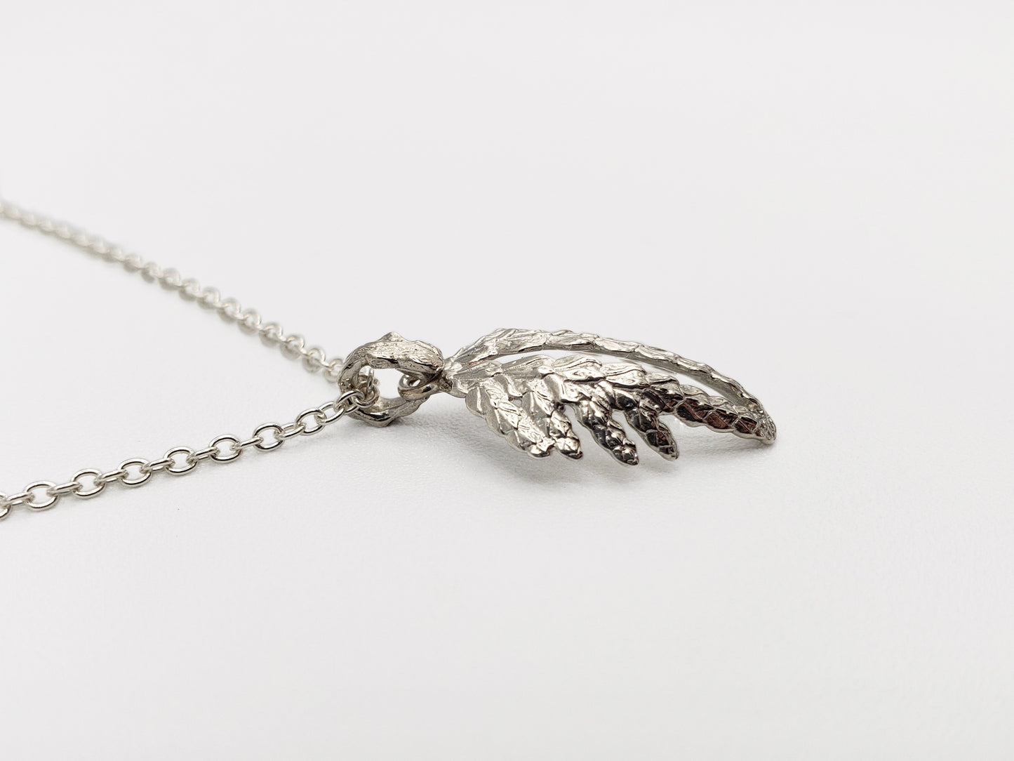 Sterling silver cedar pendant resembling wings shown at an extreme sideways angle.