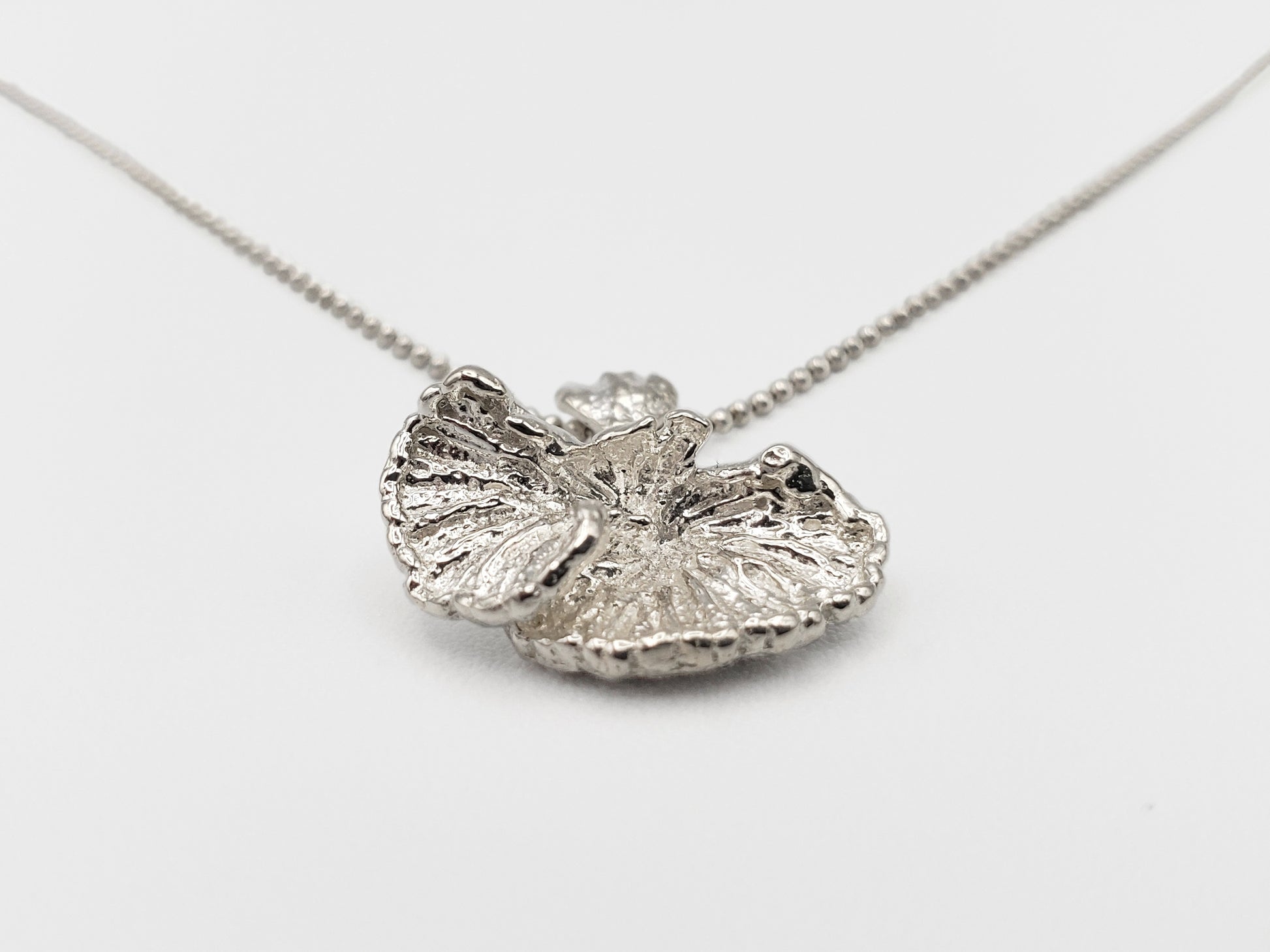 Sterling silver fungi pendant that is positioned at an extreme angle, looking up from the bottom.