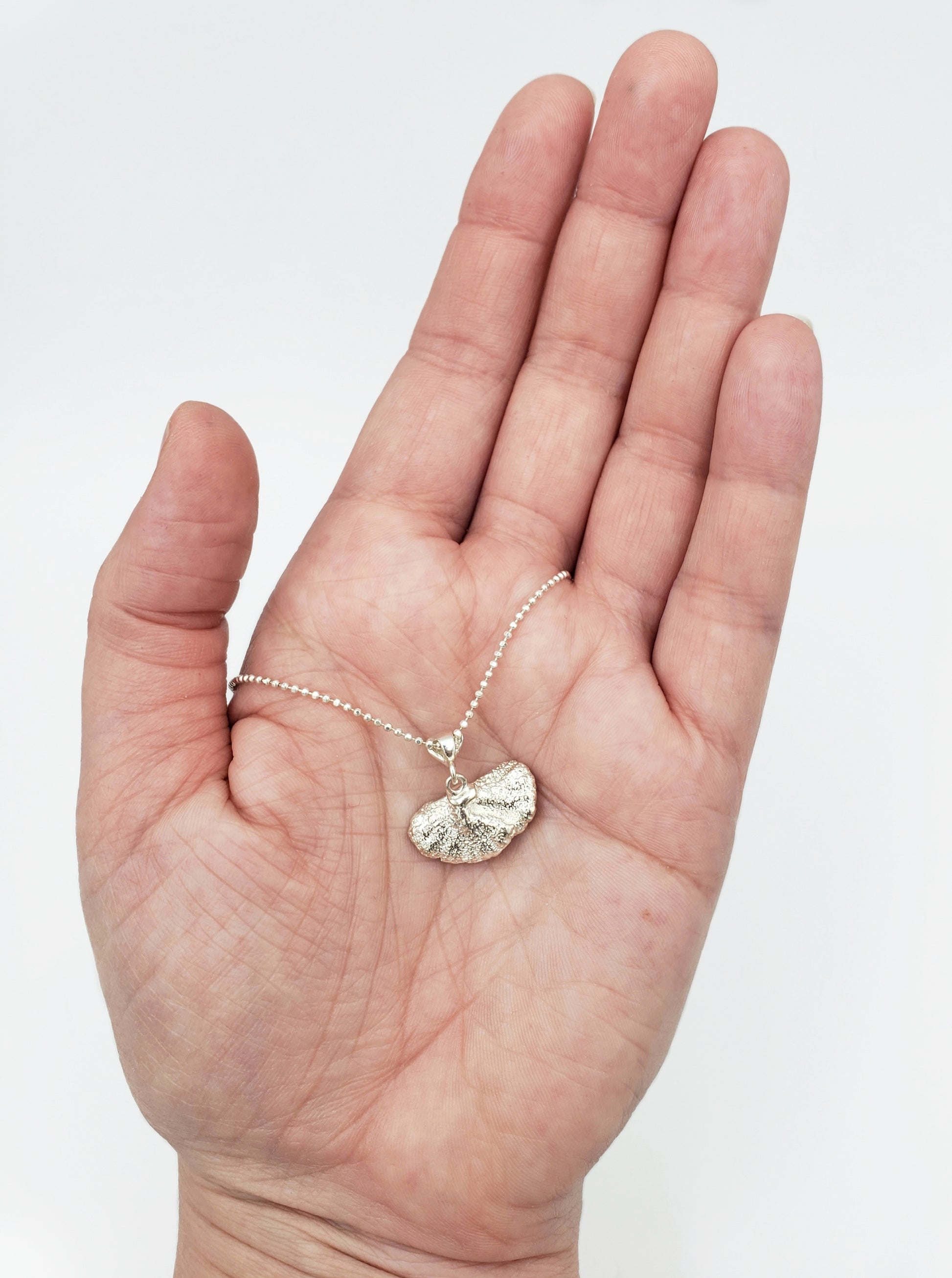 Hand holding a sterling silver fungi pendant with back of pendant showing.