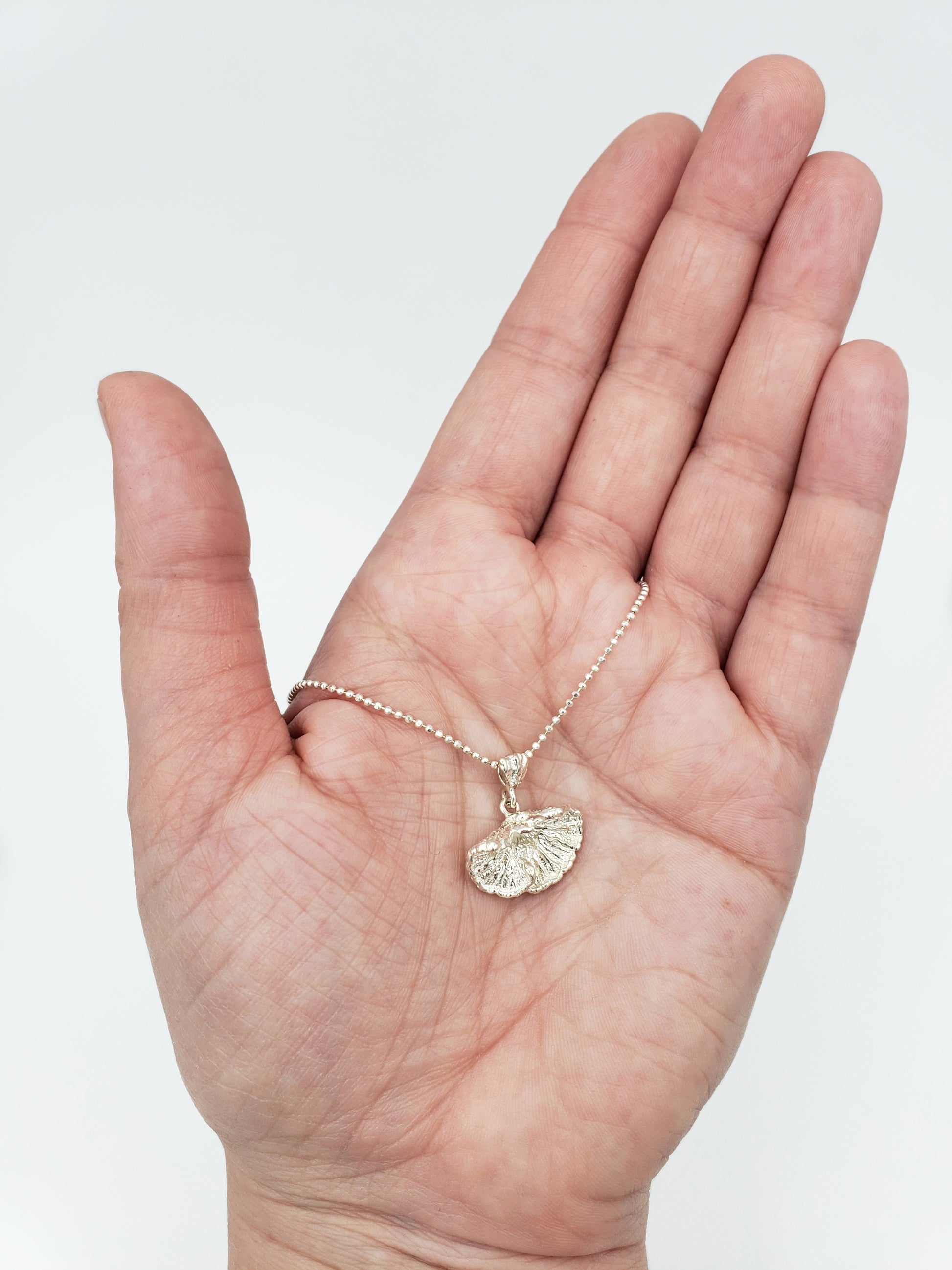 Hand holding sterling silver fungi pendant.