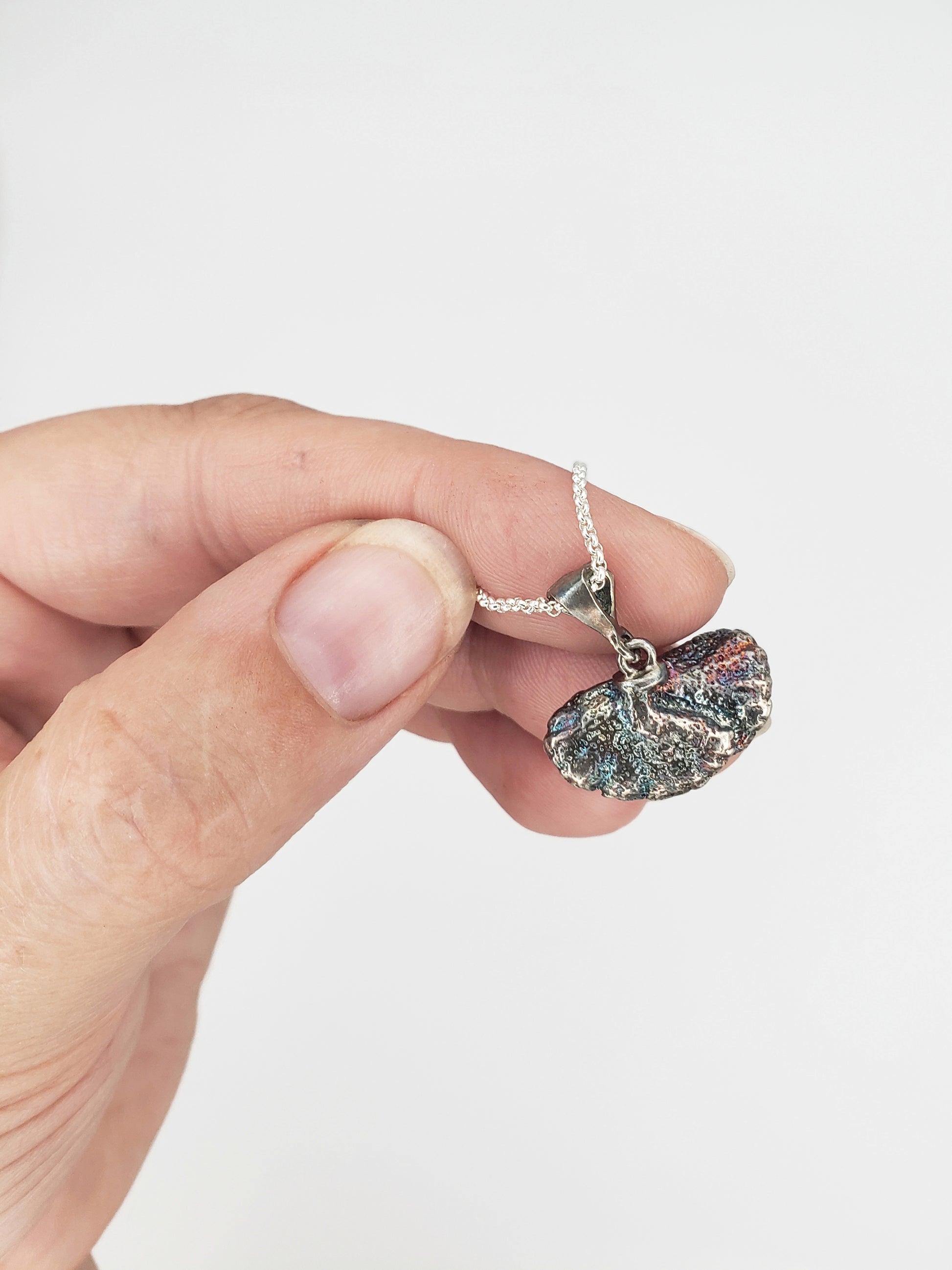 Hand holding an oxidized sterling silver fungi pendant, showing the back of the pendant.