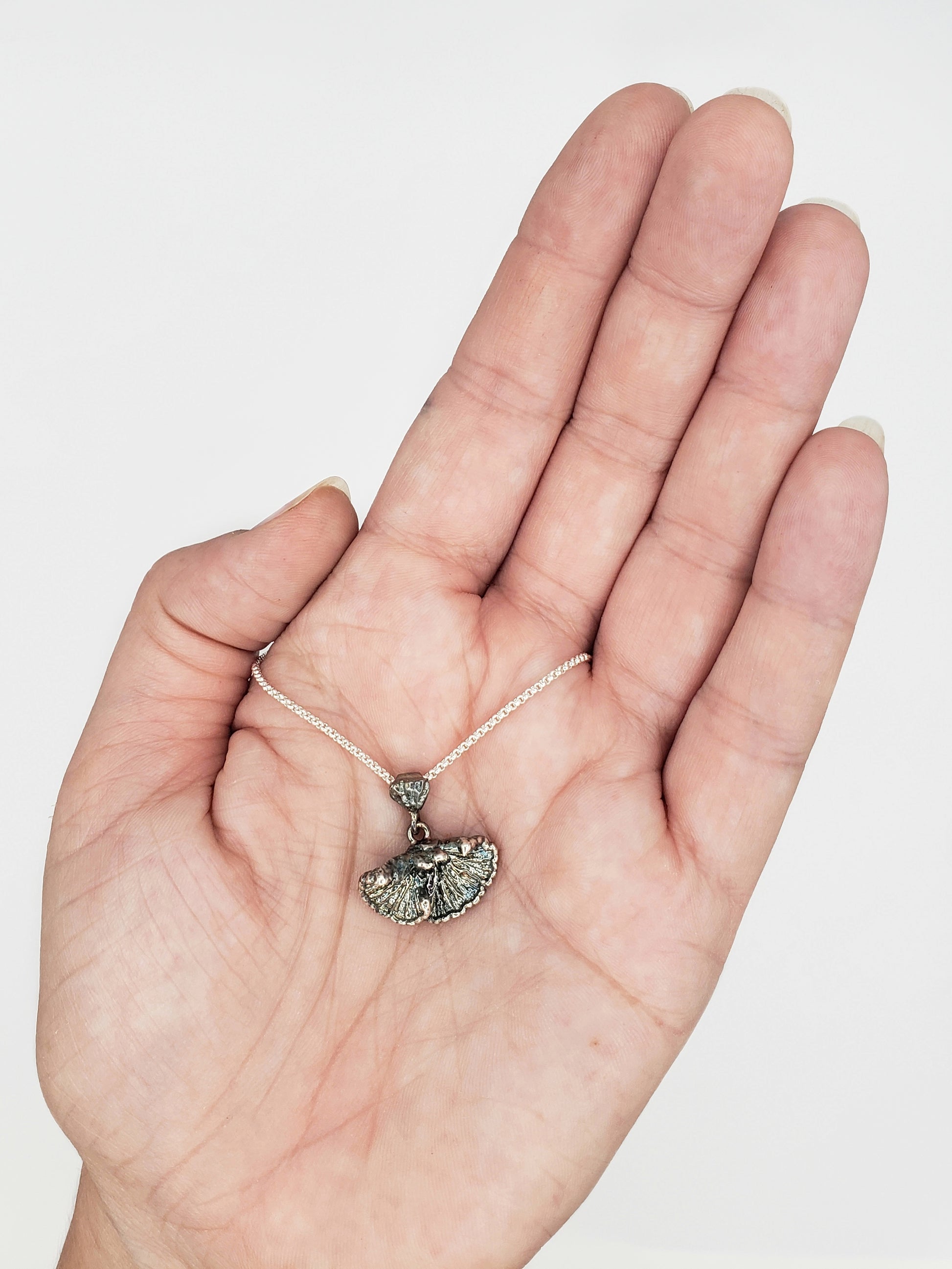 Hand holding an oxidized sterling silver fungi pendant.