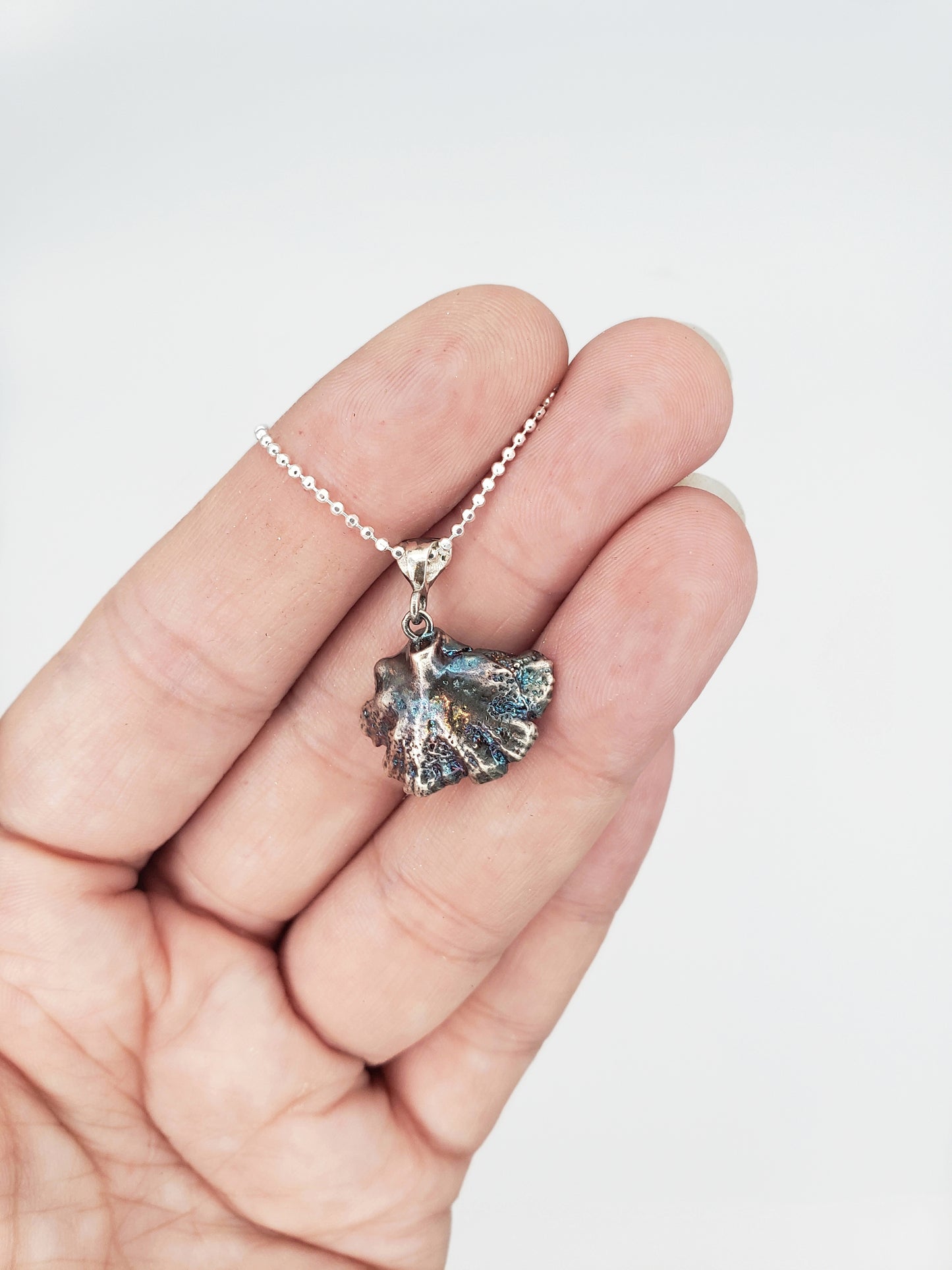 Hand holding an oxidized sterling silver fungi pendant with a ruffled edge. Back of pendant is facing forward.