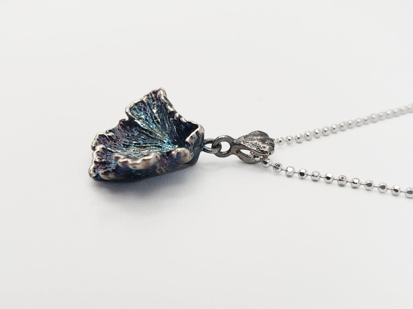 Oxidized sterling silver fungi pendant with ruffled edge. Shown at a sideways angle.