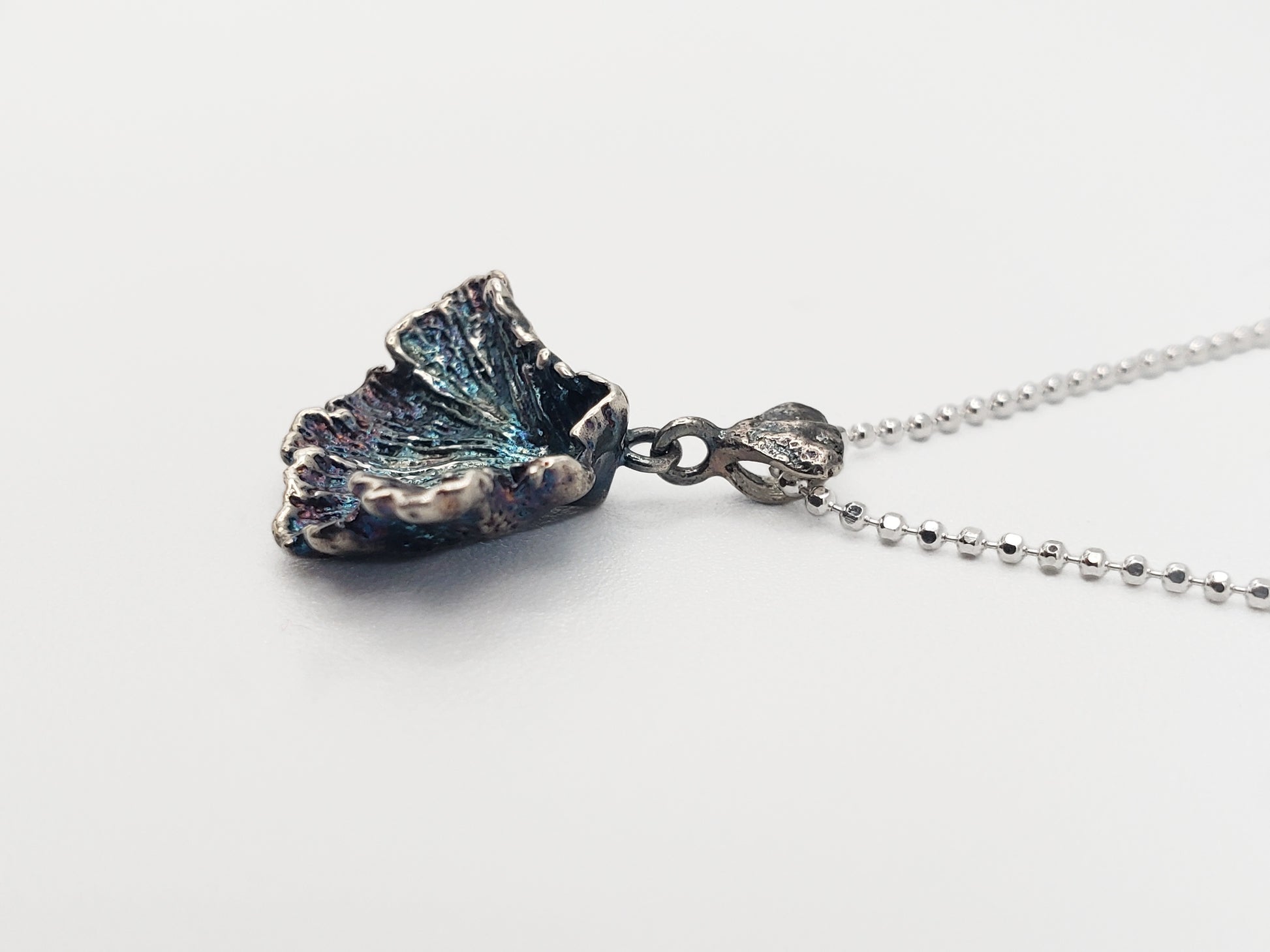 Oxidized sterling silver fungi pendant with ruffled edge. Shown at a sideways angle.