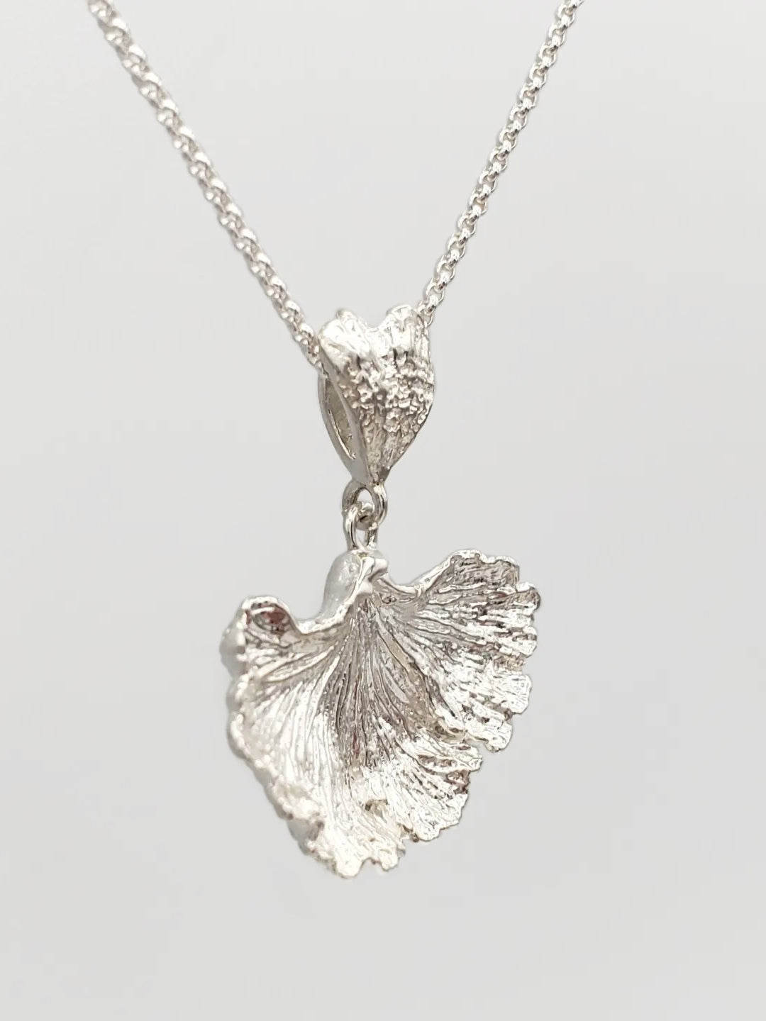 Sterling silver fungi pendant with a ruffled edge and gills showing. Shown at a sideways angle.