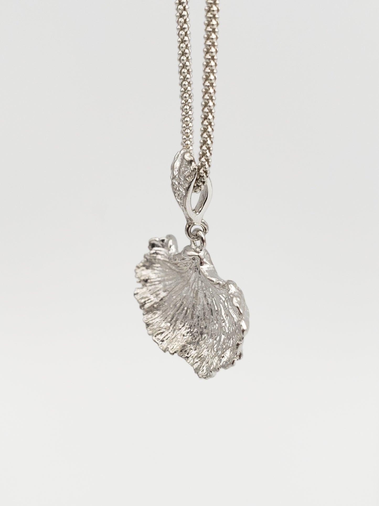 Sterling silver fungi pendant with a ruffled edge and gills showing. Shown at an extreme sideways angle.