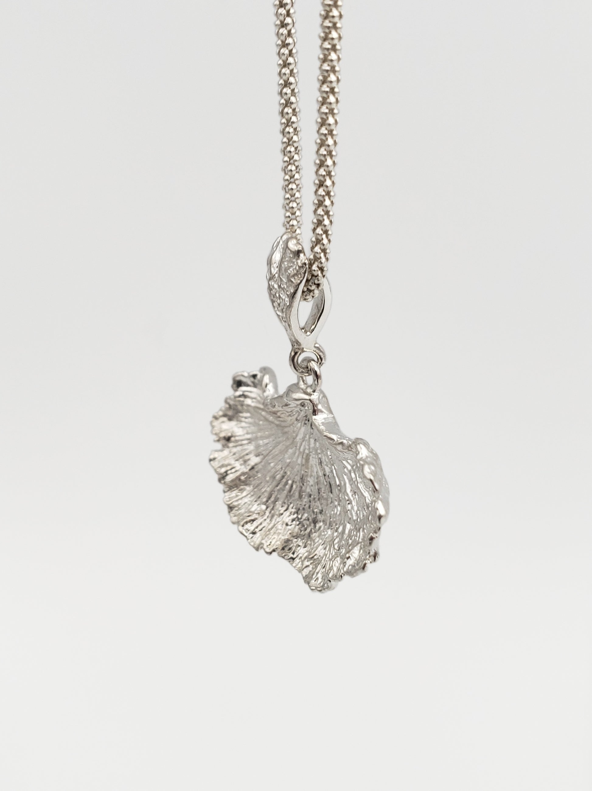 Sterling silver fungi pendant with a ruffled edge and gills showing. Shown at an extreme sideways angle.