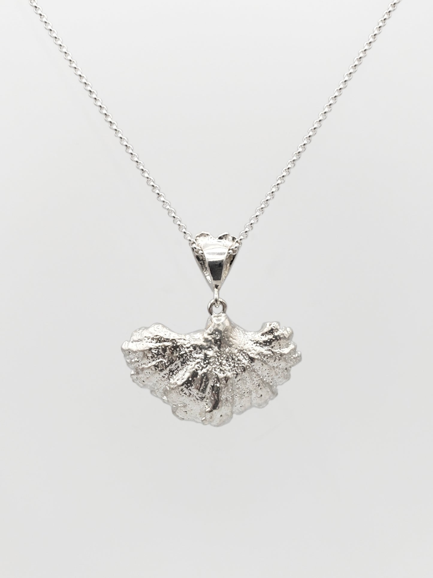 Sterling silver fungi pendant with a ruffled edge and gills showing. Shown with the back of the pendant is facing forward.