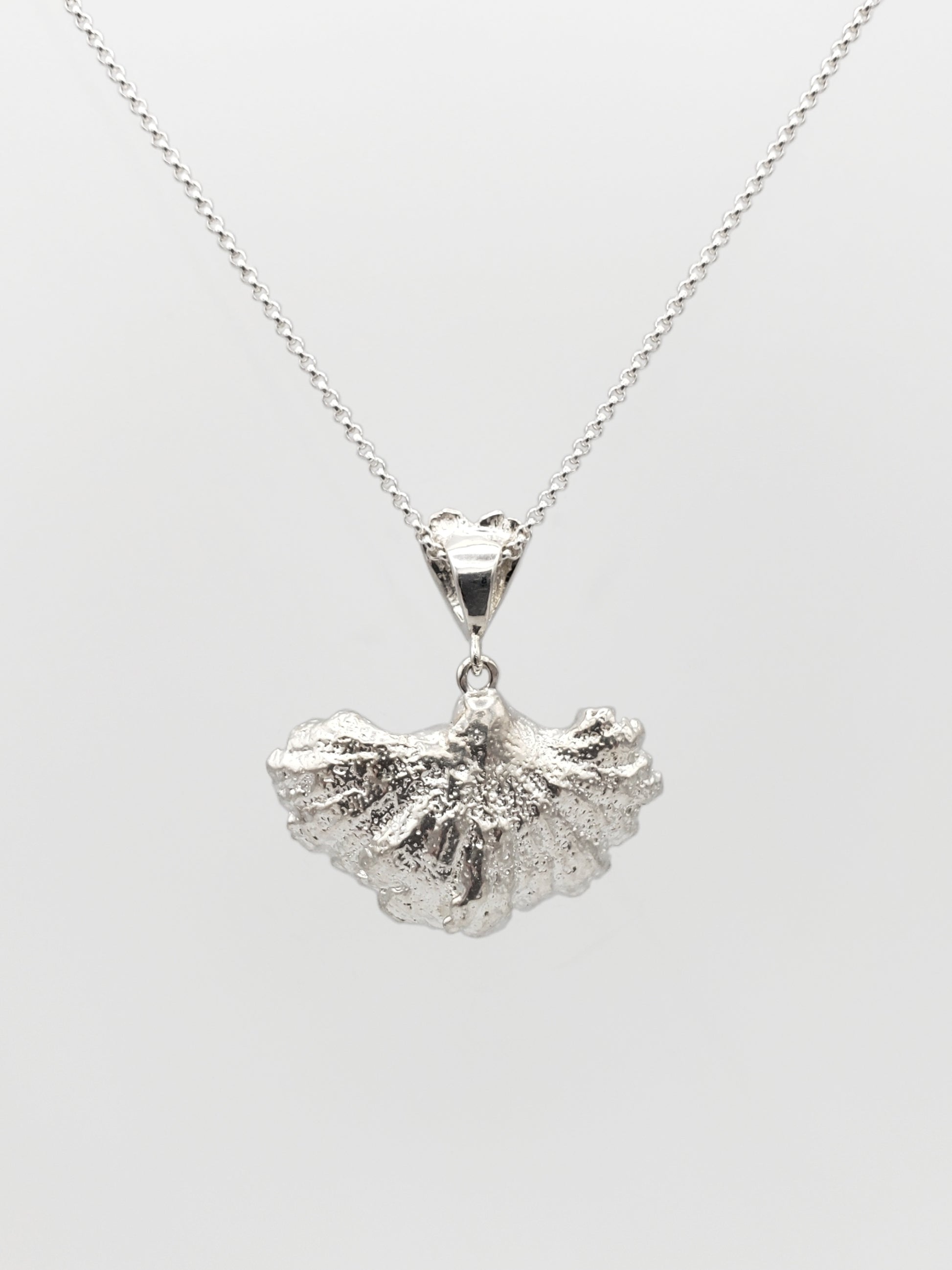 Sterling silver fungi pendant with a ruffled edge and gills showing. Shown with the back of the pendant is facing forward.