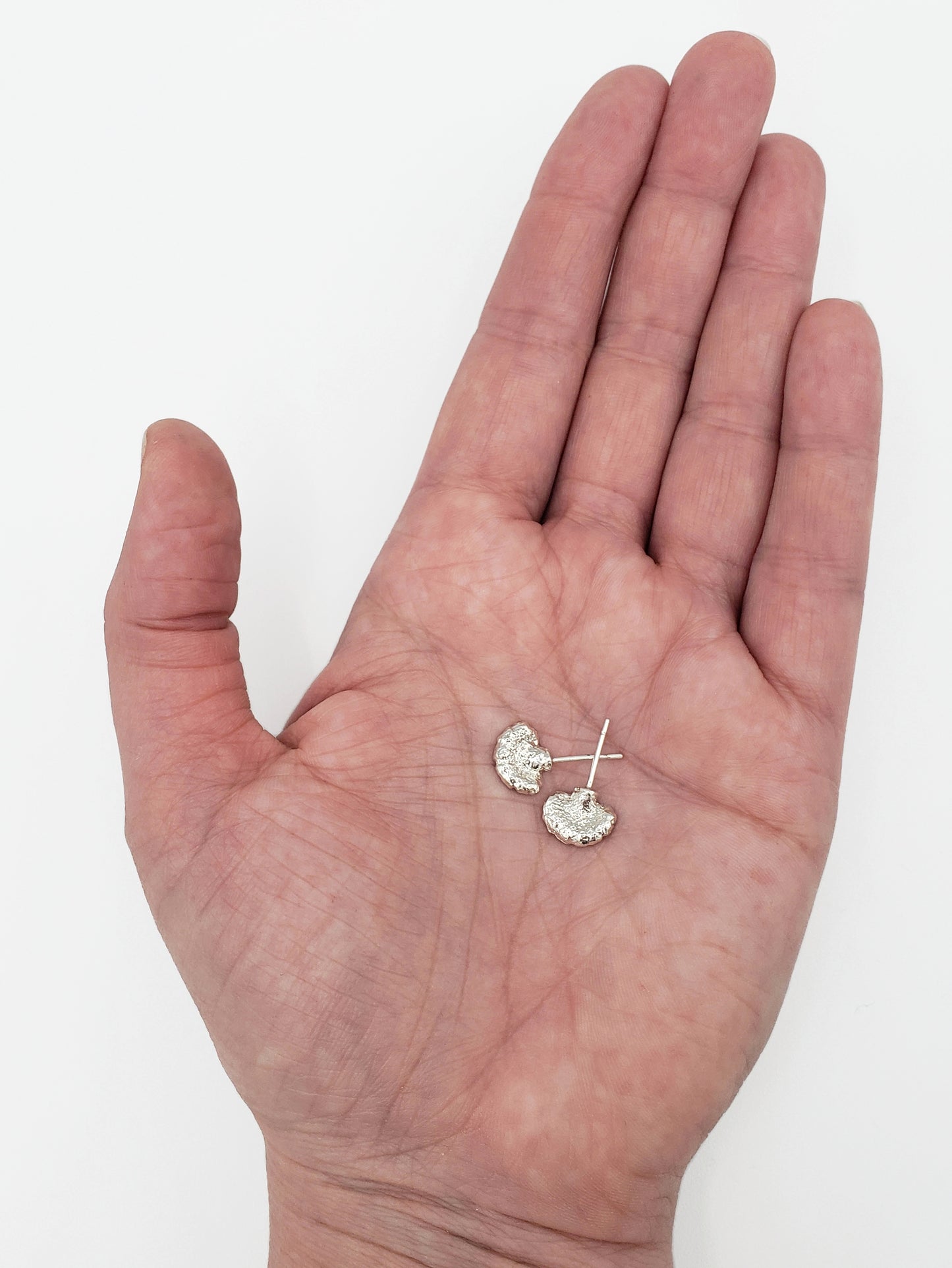 Sterling silver fungi stud earrings held in a hand without the butterfly backs.
