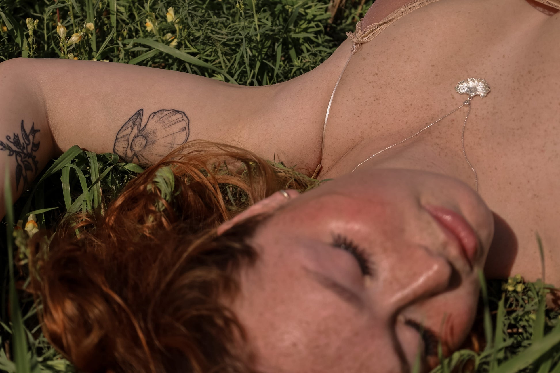 Red haired woman laying in grass wearing a sterling silver fungi pendant.