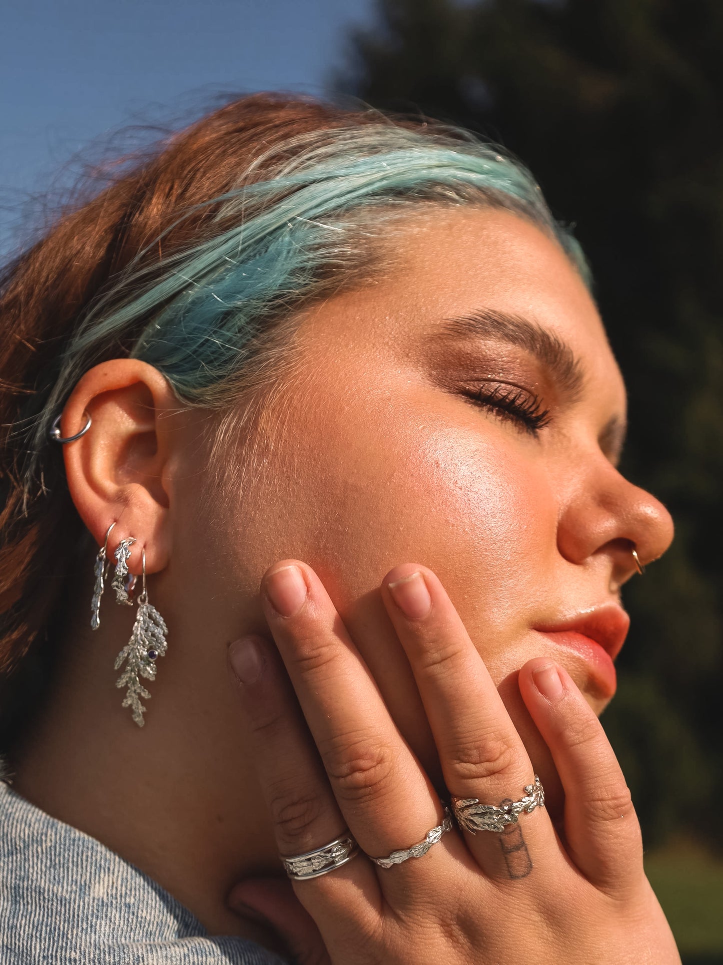Woman with her hand on her face wearing sterling silver jewellery / jewelry. Including cedar hoop earrings, cedar dangle earrings and cedar rings.