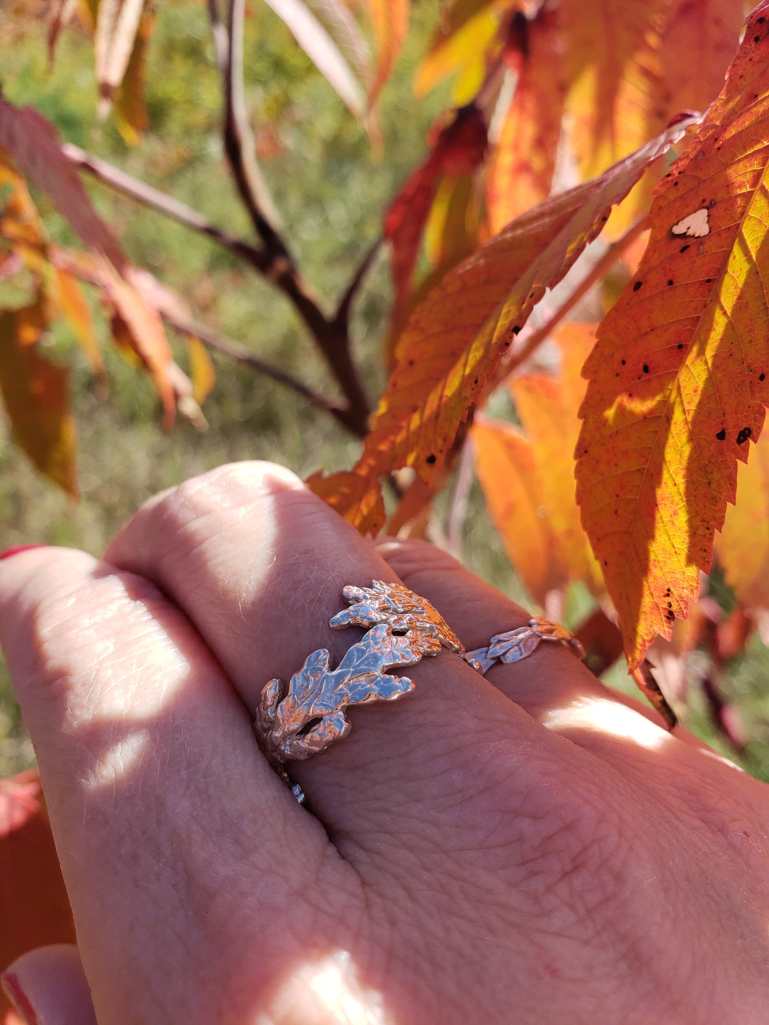 A hand wearing two silver rings made from cedar. Orange sumac leaves are in the background.