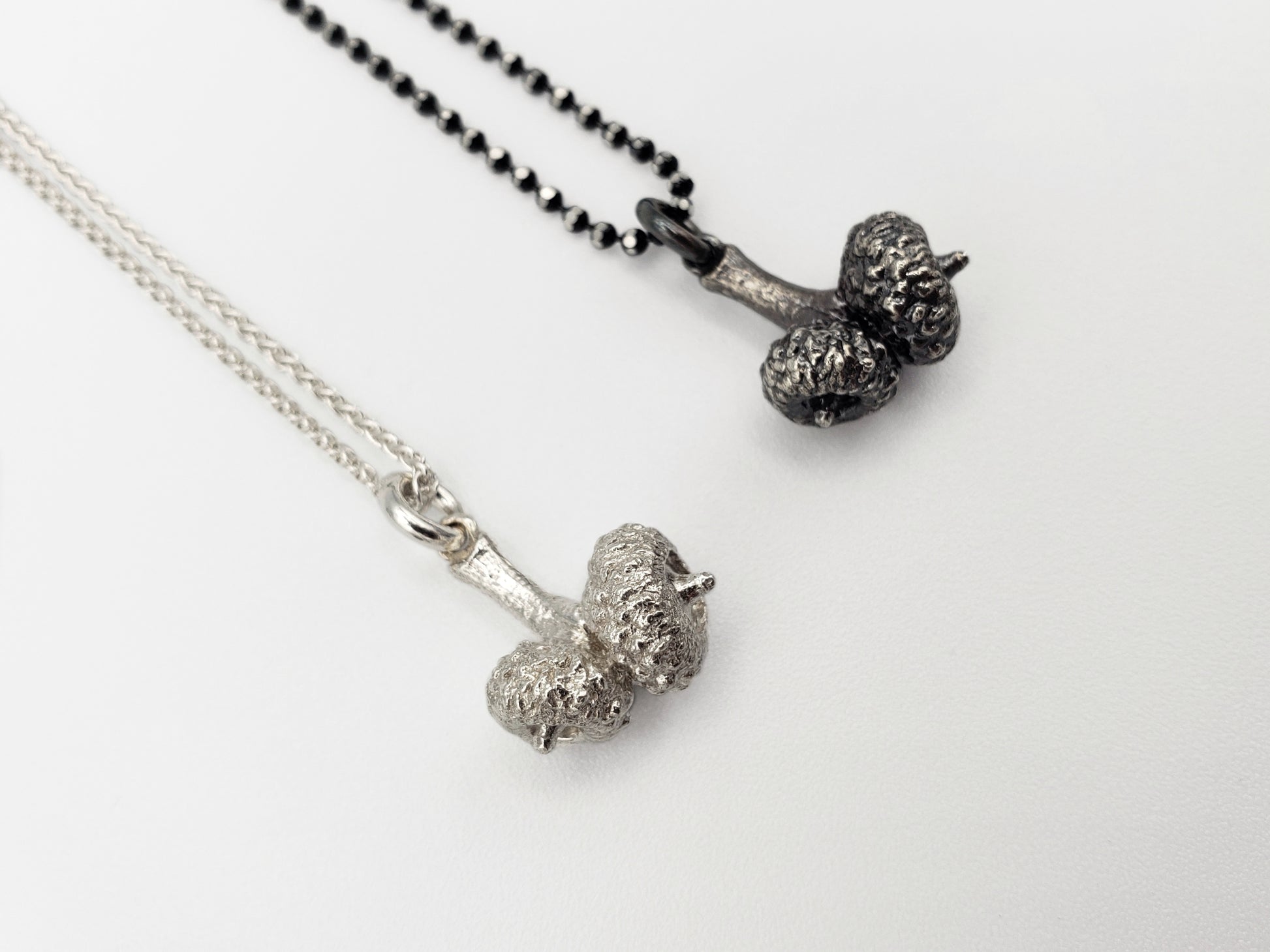 Two silver double acorn pendants. One silver colour, the other oxidized grey colour 