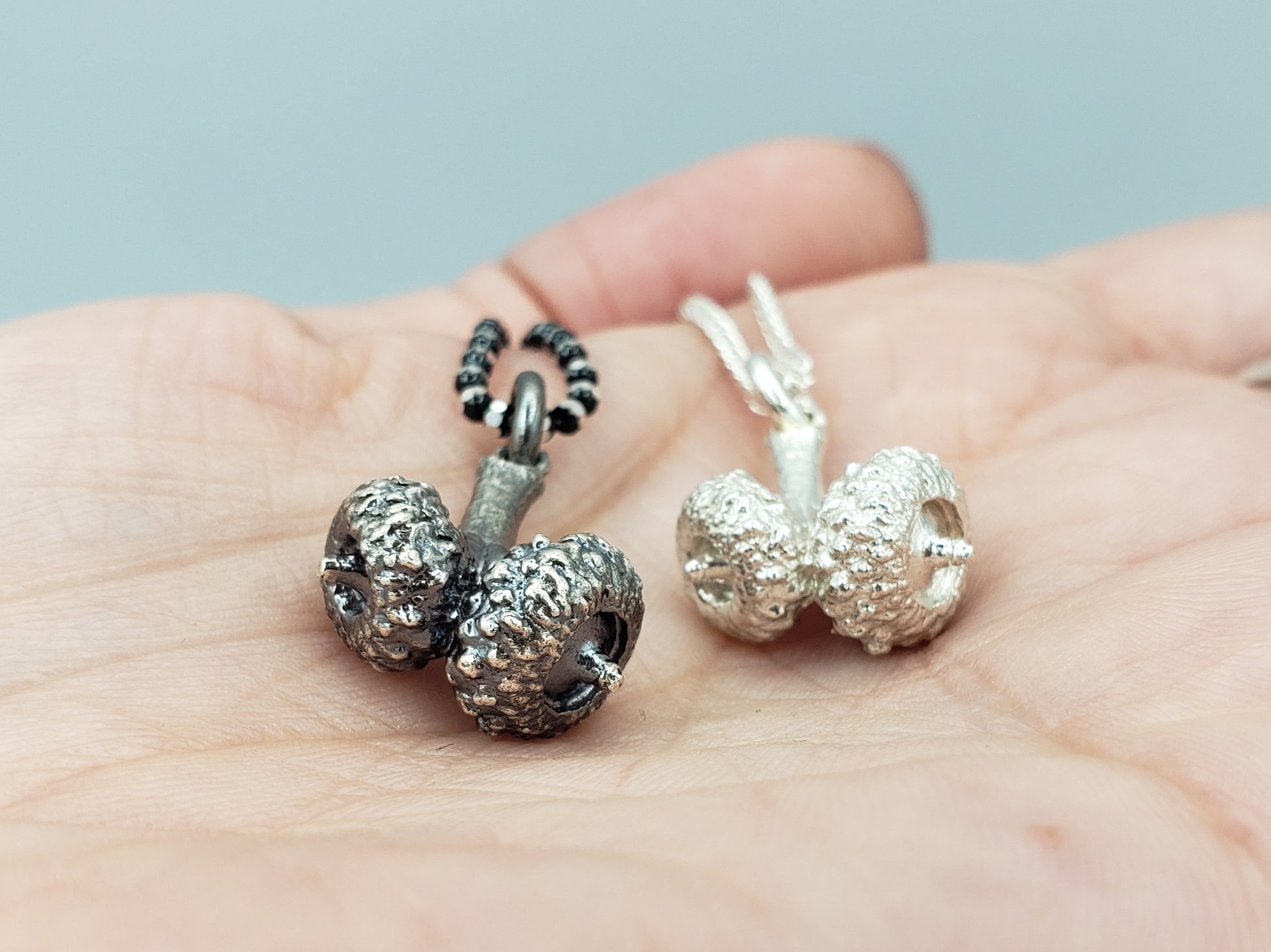 Two silver double acorn pendants. One silver colour, the other oxidized grey colour 