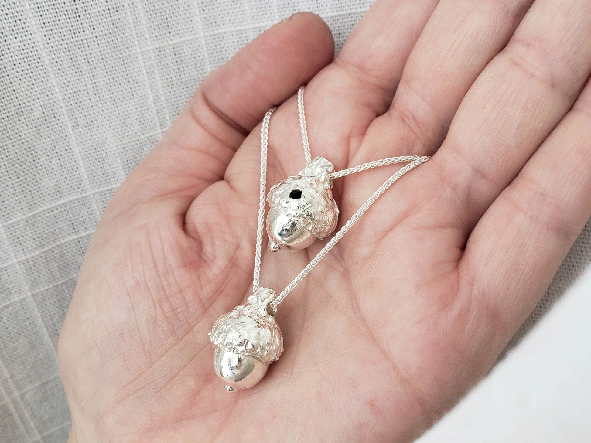 Two silver acorn pendants. One has a hole in the cap.