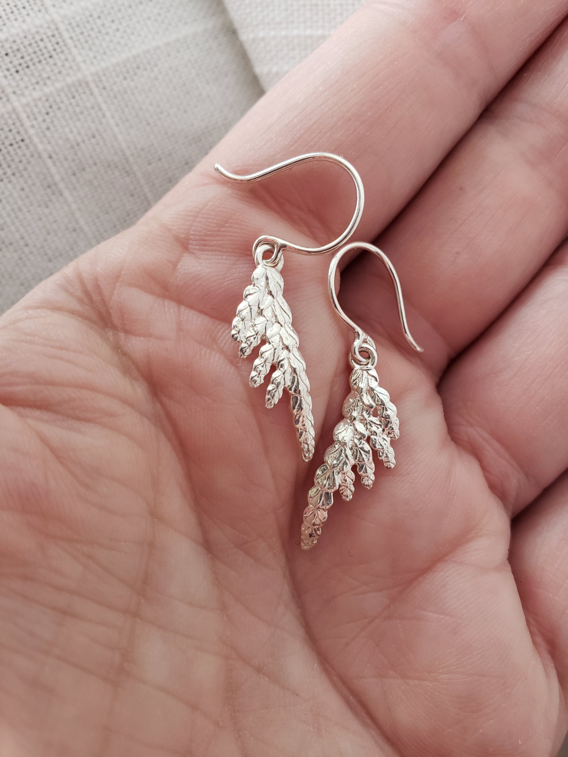 Hand holding a pair of sterling silver cedar dangle earrings.