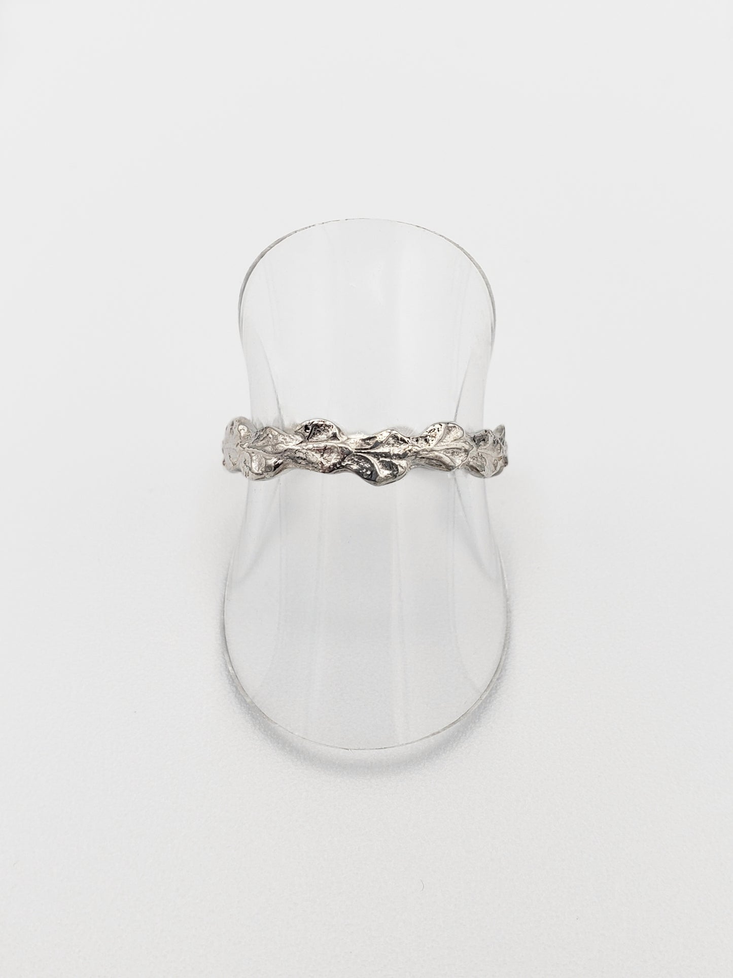 Narrow sterling silver cedar ring. Displayed on a clear vinyl stand.