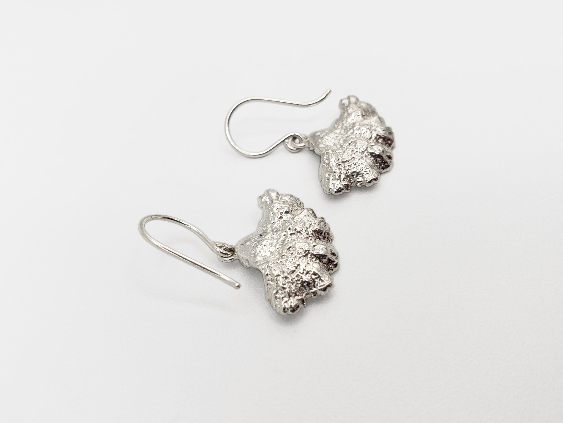 Sterling silver fungi earrings with a ruffled edge, shown upside down so the back is showing.