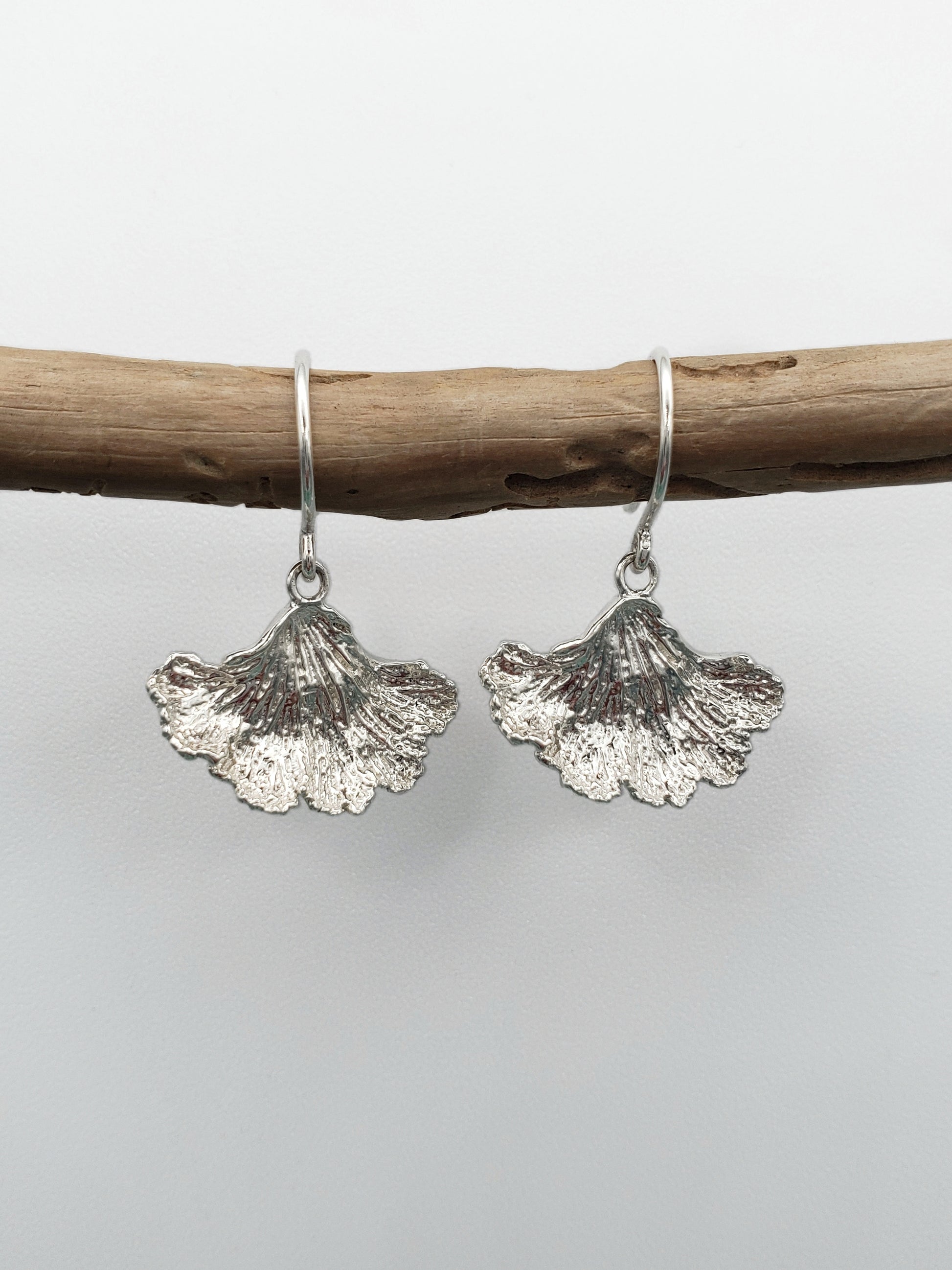 Sterling silver fungi earrings with a ruffled edge. Displayed hanging from a stick.