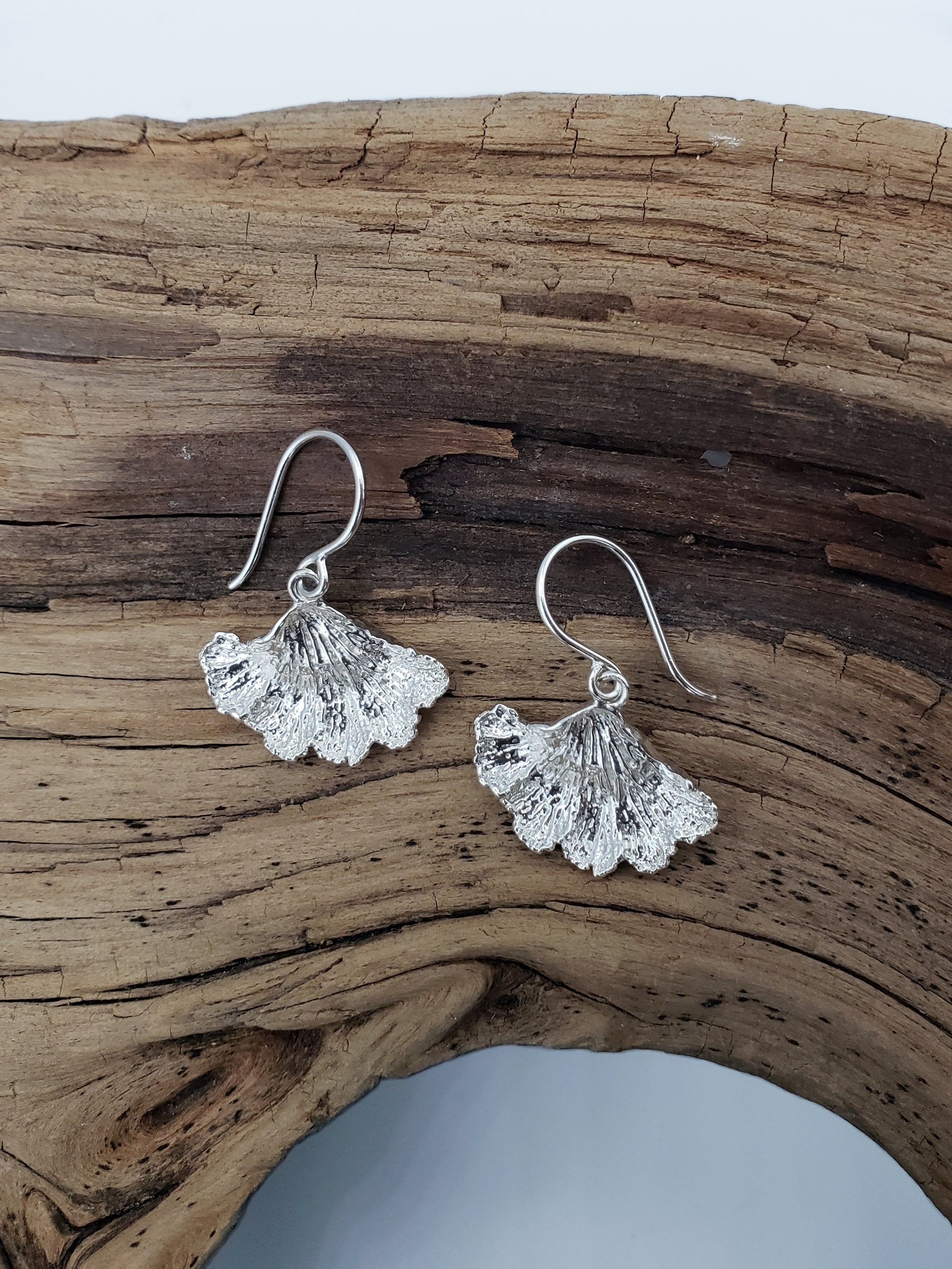 Sterling silver fungi earrings with a ruffled edge on top of wood.