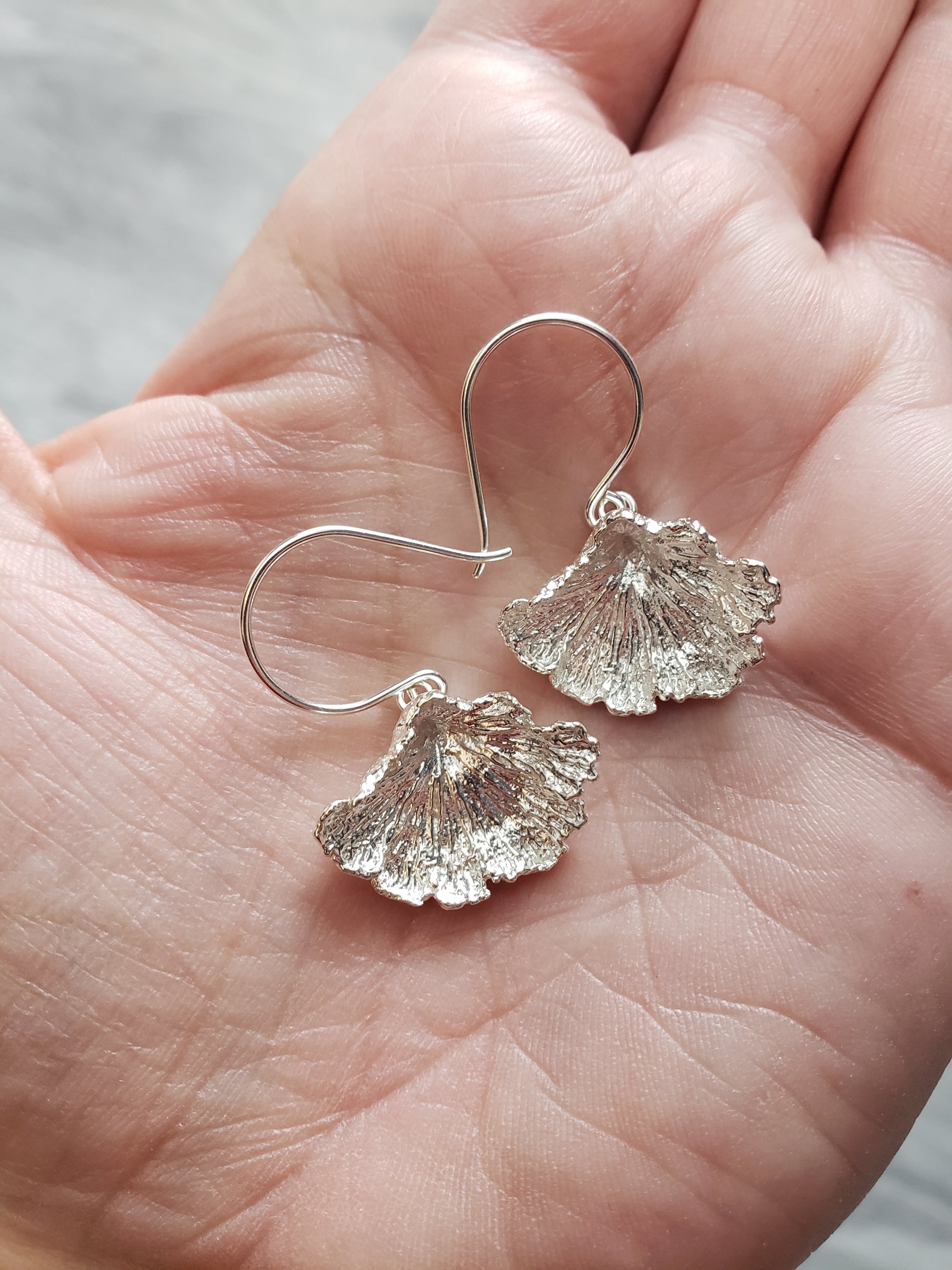 Hand holding a pair of sterling silver fungi earrings with a ruffled edge.