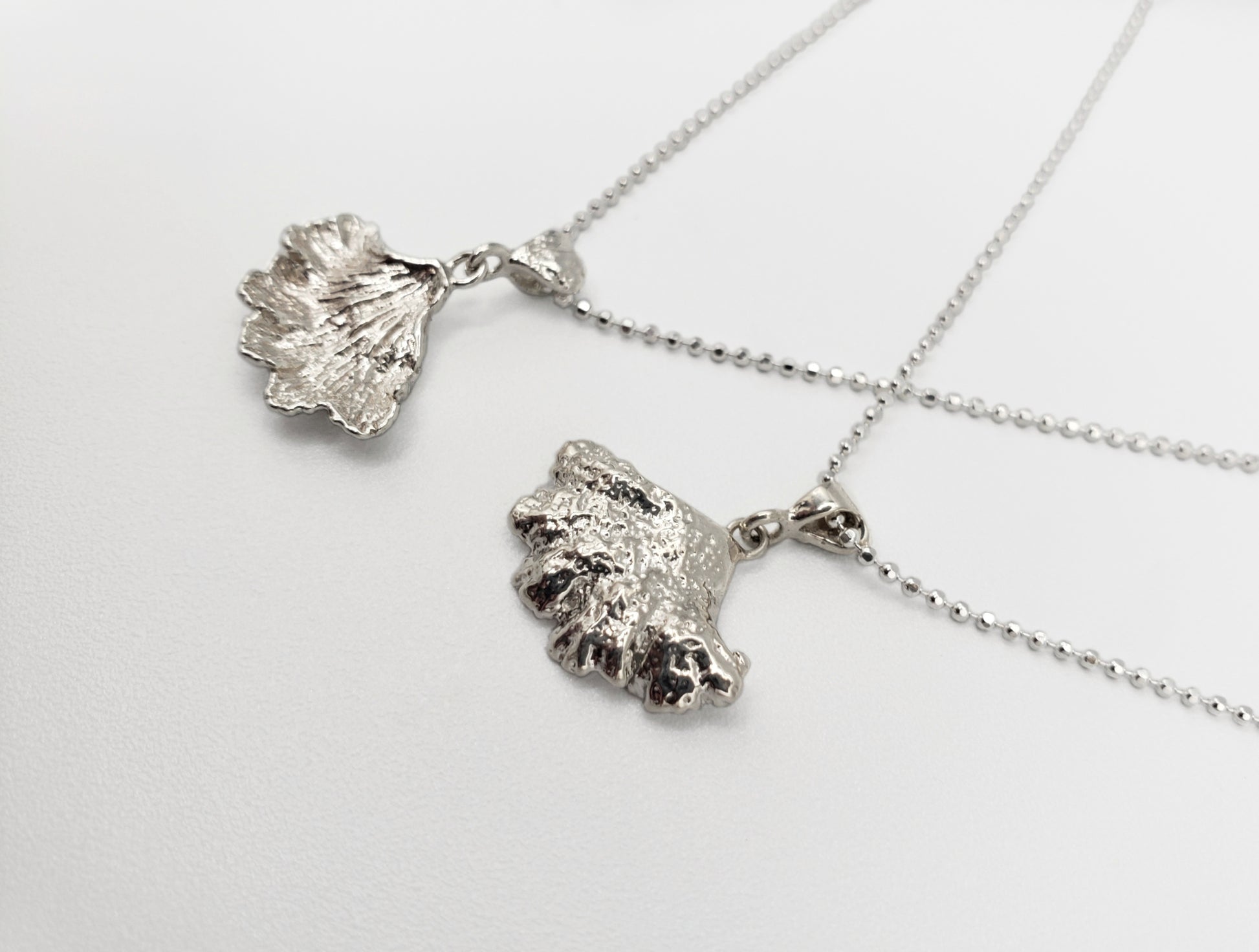 Two sterling silver fungi pendants. Displayed to show both front & back of pendants from a side angle.