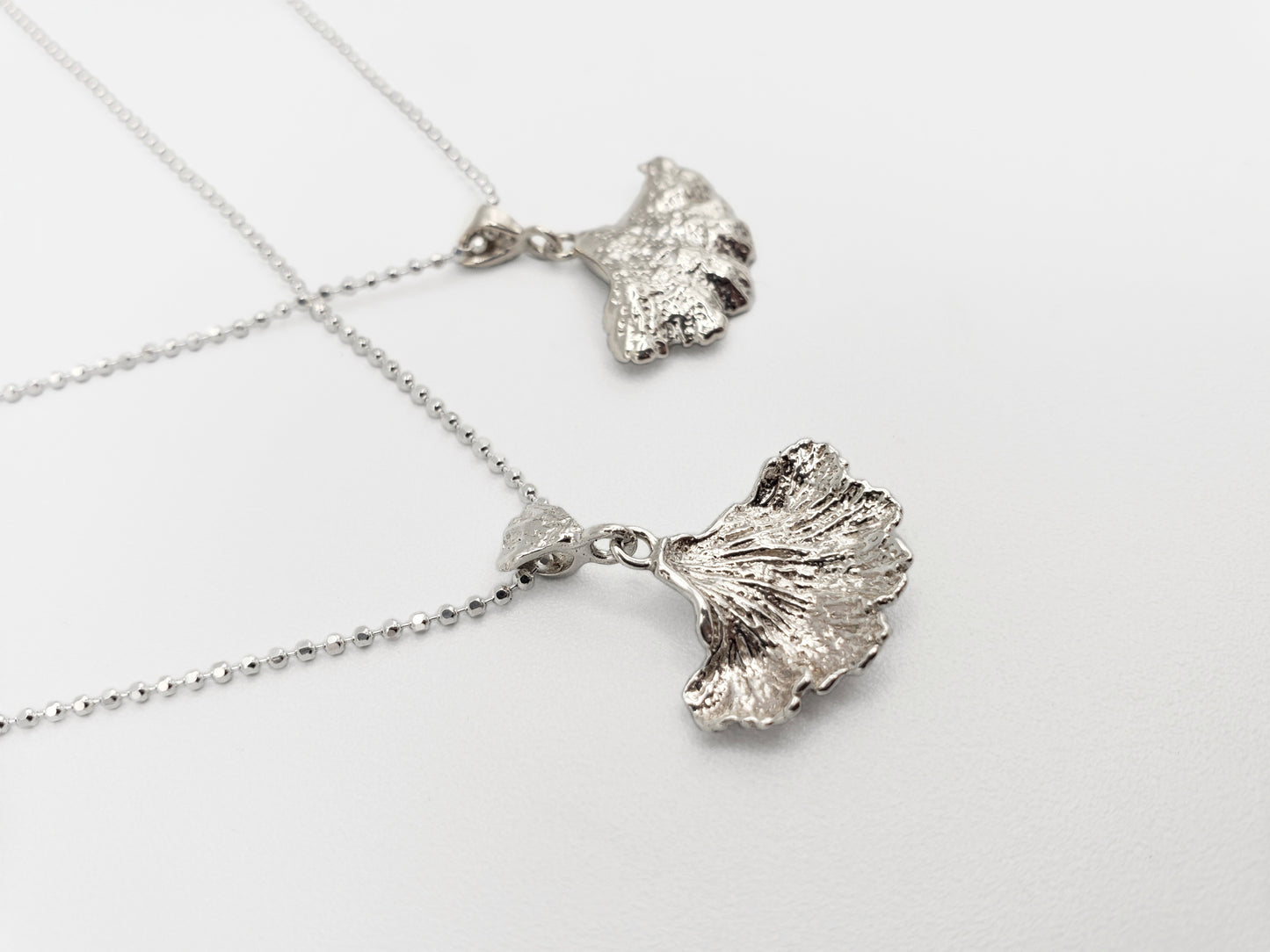 Two sterling silver fungi pendants. Displayed to show both front & back of pendants from a side angle.