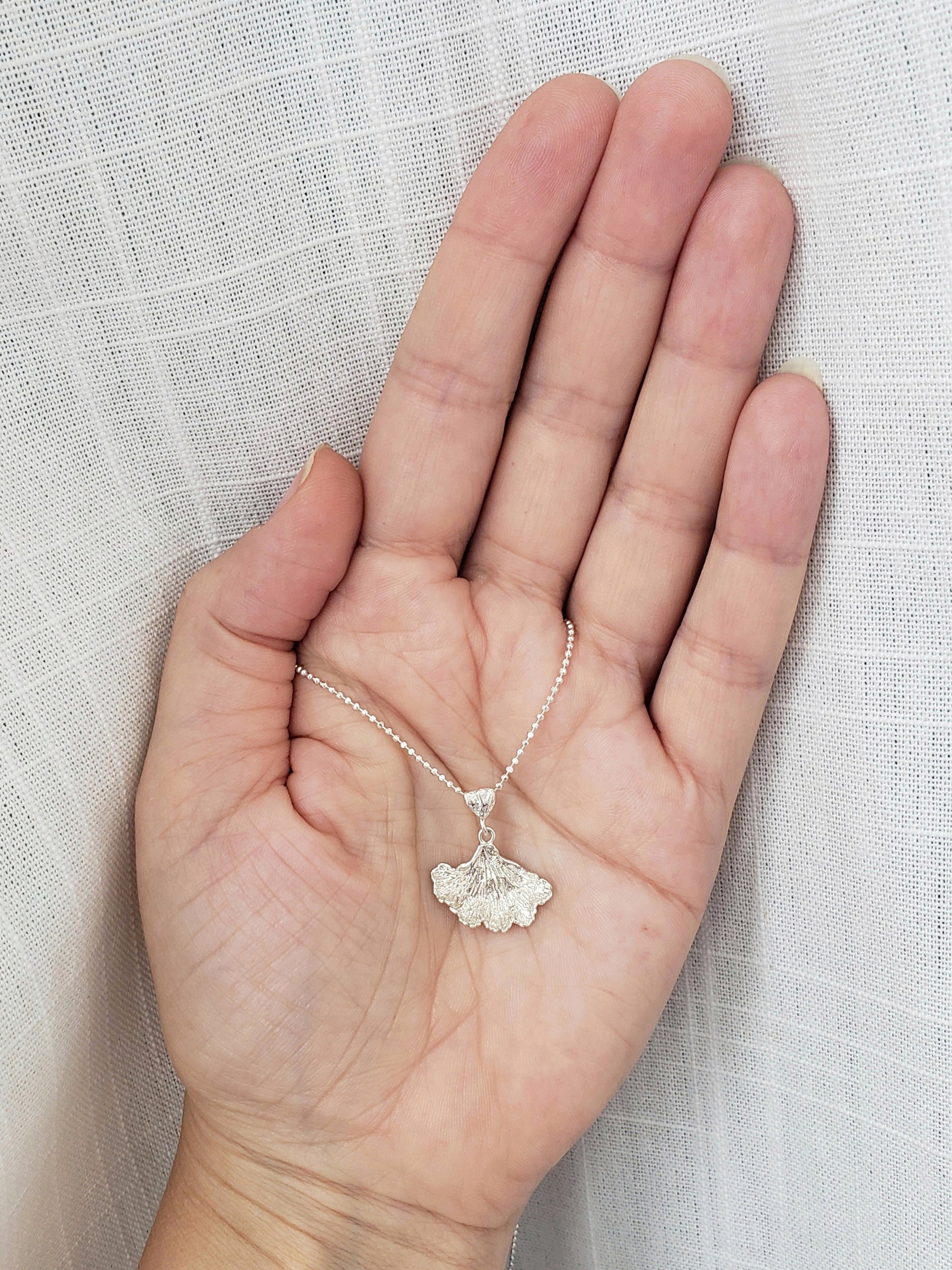 Hand holding sterling silver fungi pendant in front of white fabric.