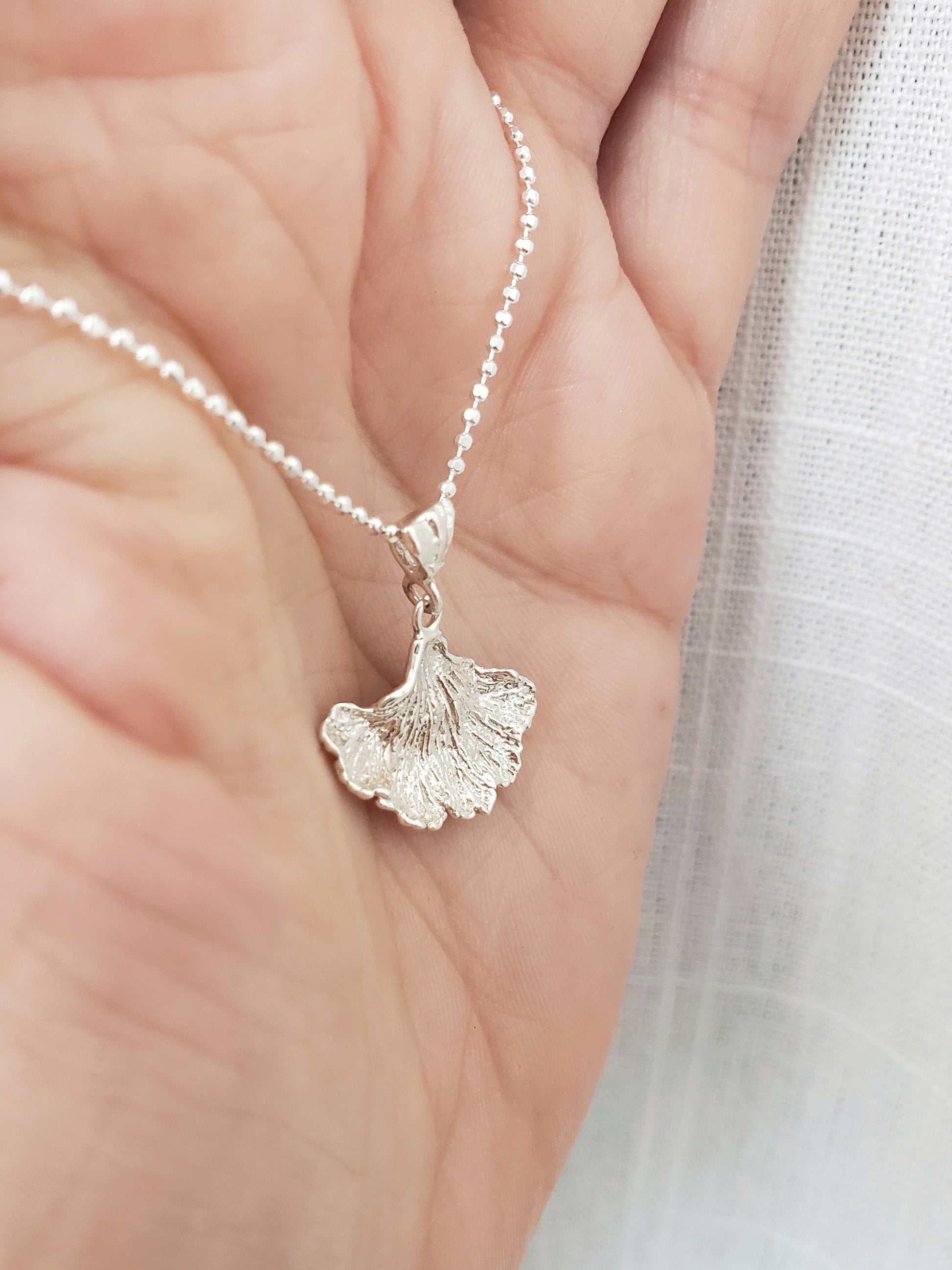 Sterling silver fungi pendant held in front of white fabric.