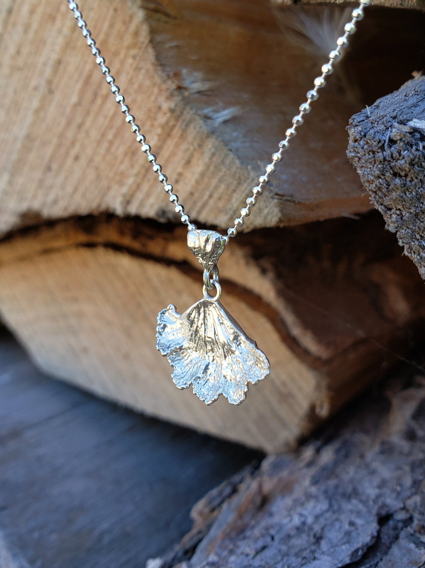 Sterling silver fungi pendant hanging in front of chopped wood