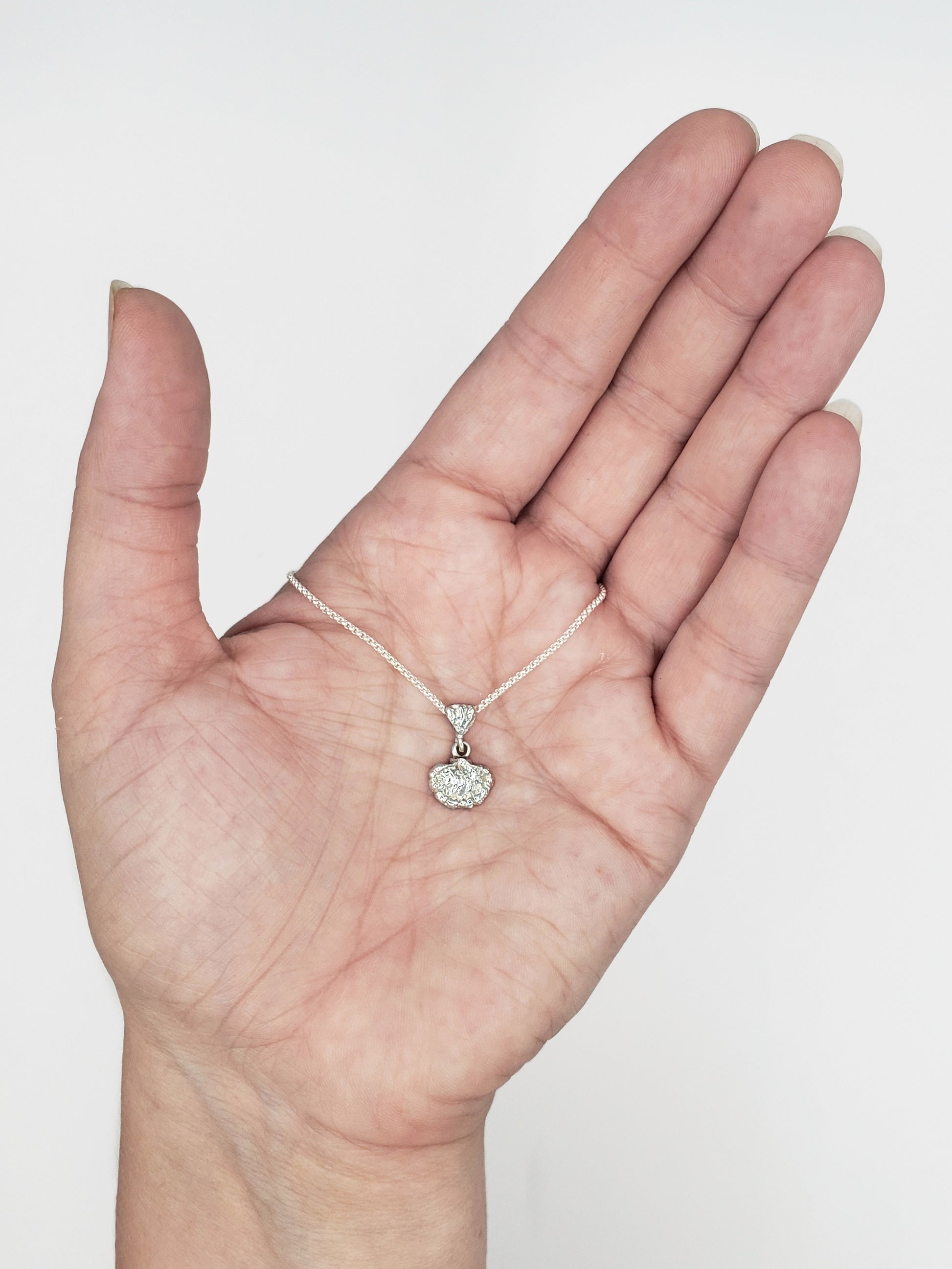 Hand holding small sterling silver fungi pendant.