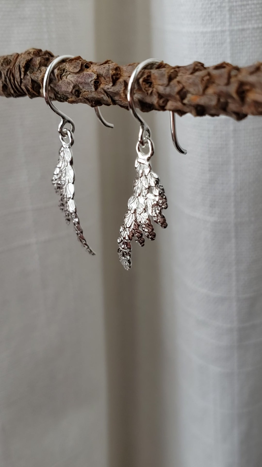 Video showing sterling silver cedar dangle earrings hanging from a stick.